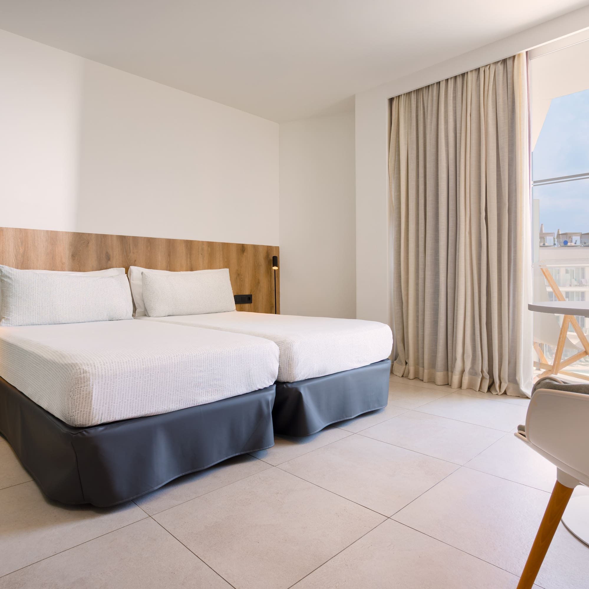 Modern hotel room with twin beds, wood headboard, and balcony.