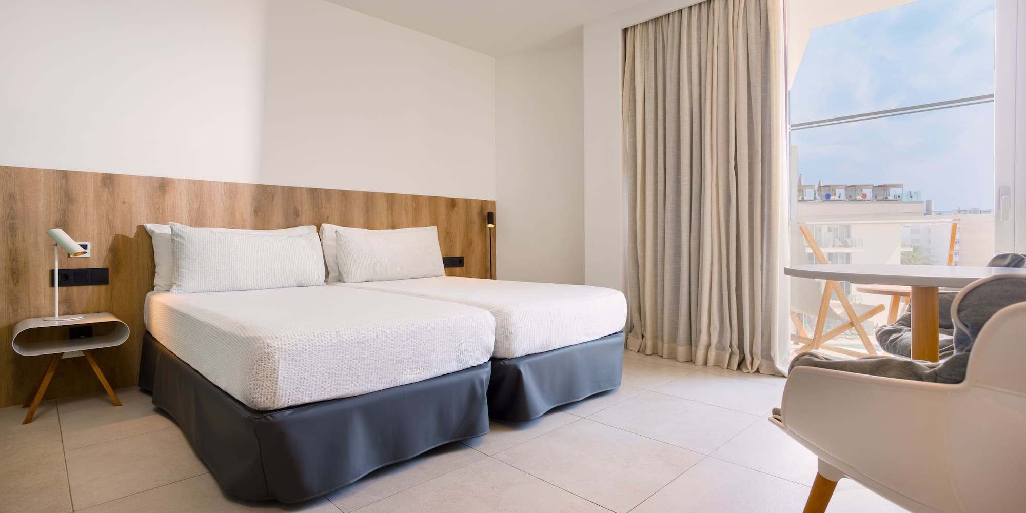 Modern hotel room with twin beds, wood headboard, and balcony.