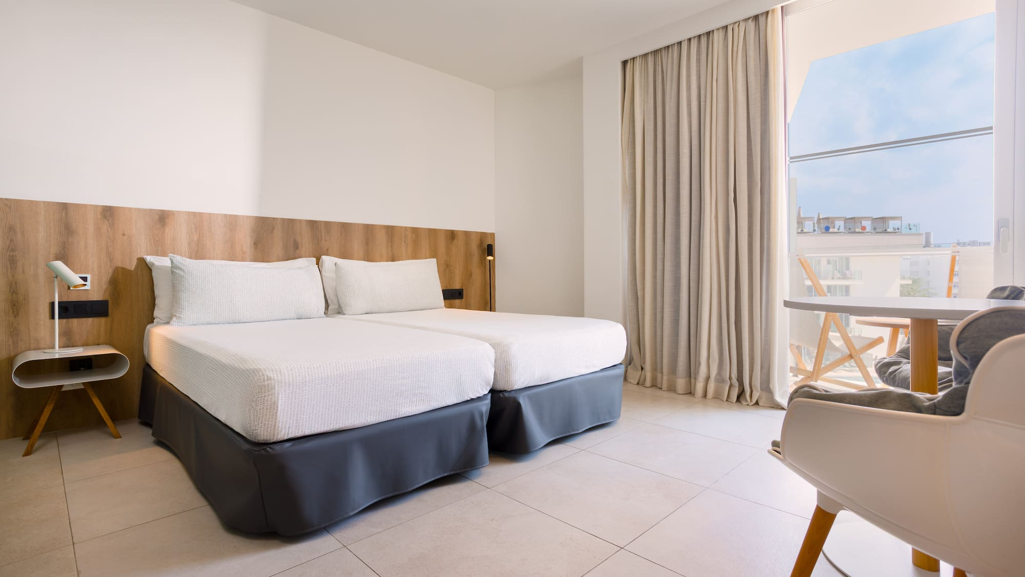 Modern hotel room with twin beds, wood headboard, and balcony.