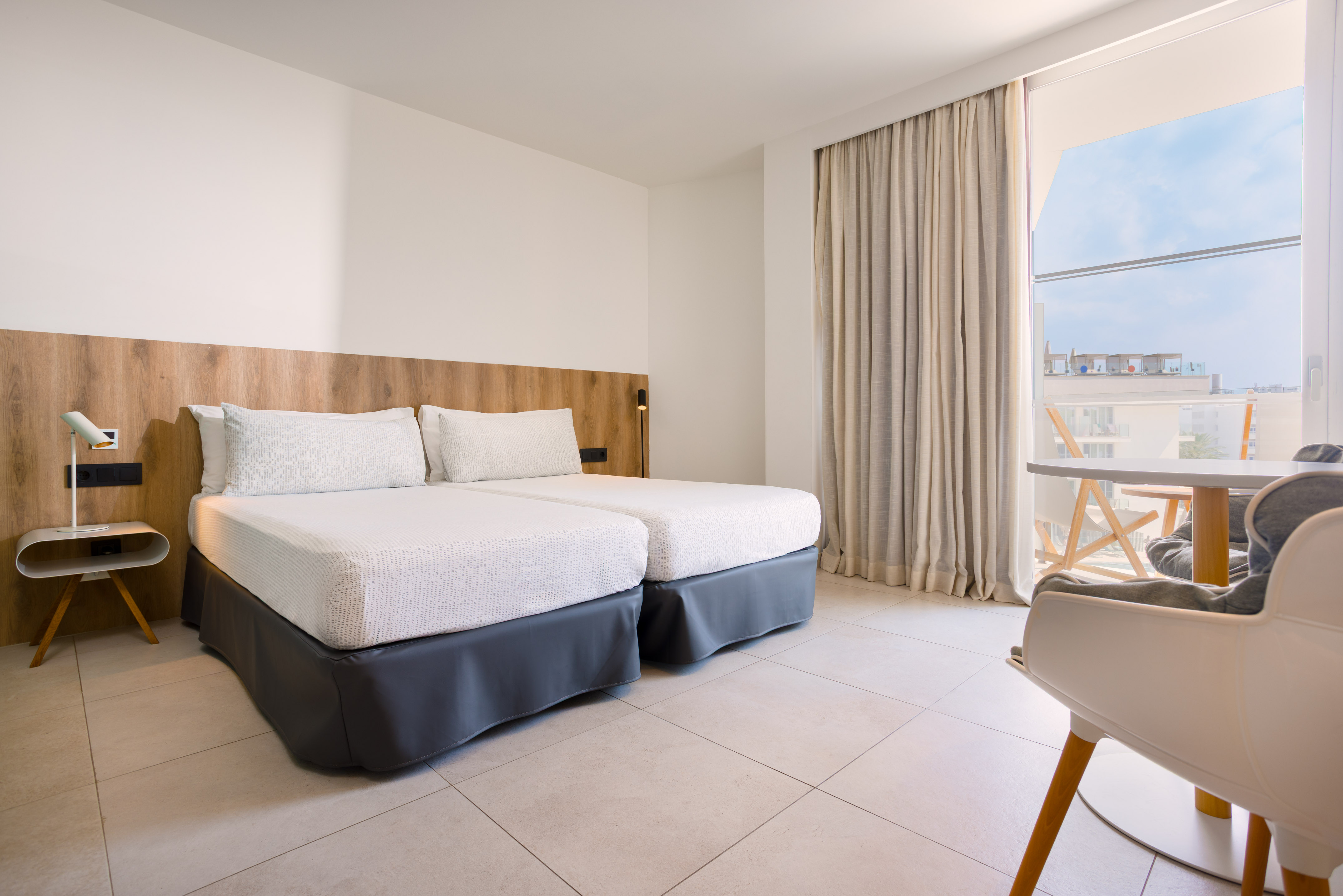 Modern hotel room with twin beds, wood headboard, and balcony.