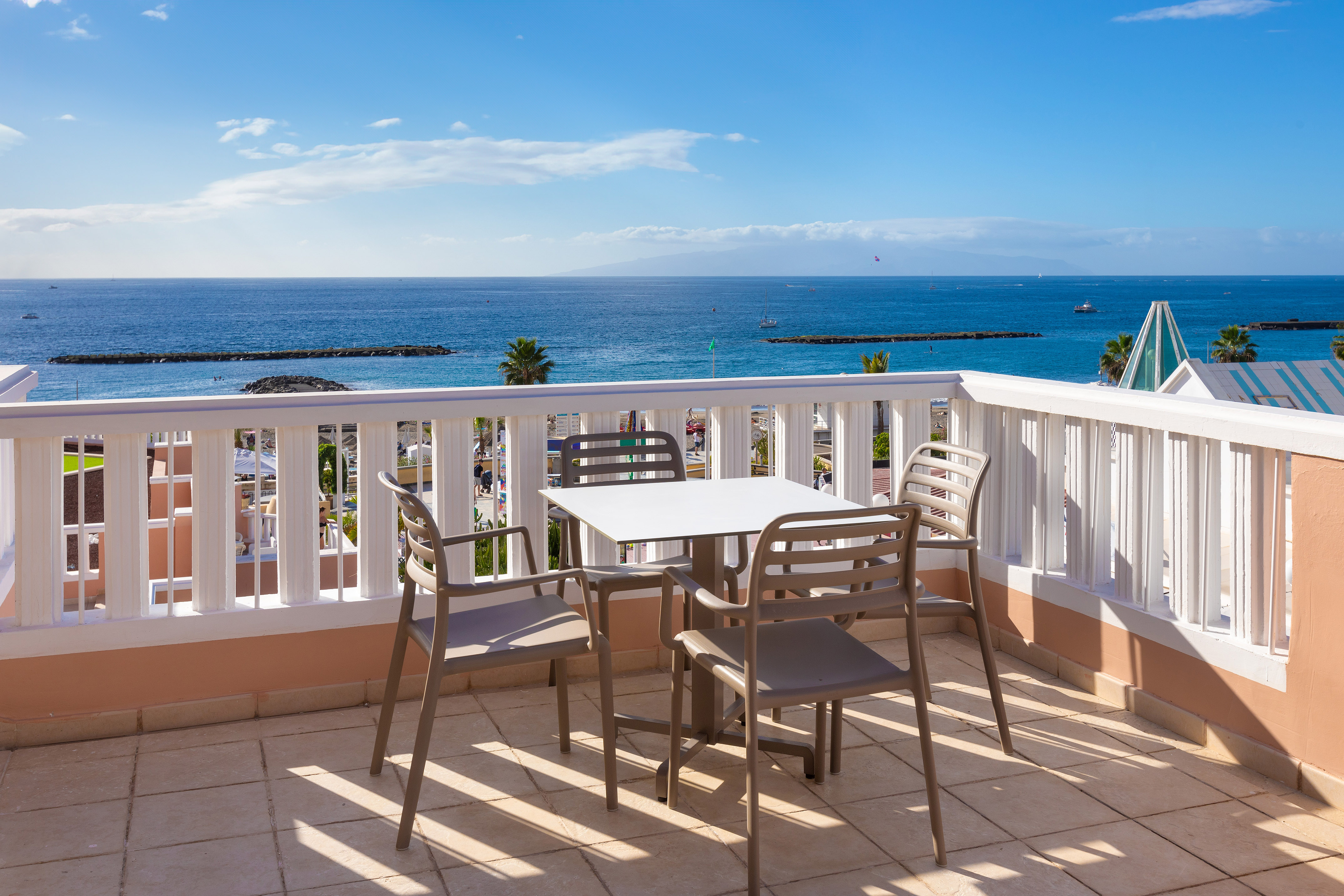 Hotel balcony with ocean view, outdoor table, and chairs under blue sky.