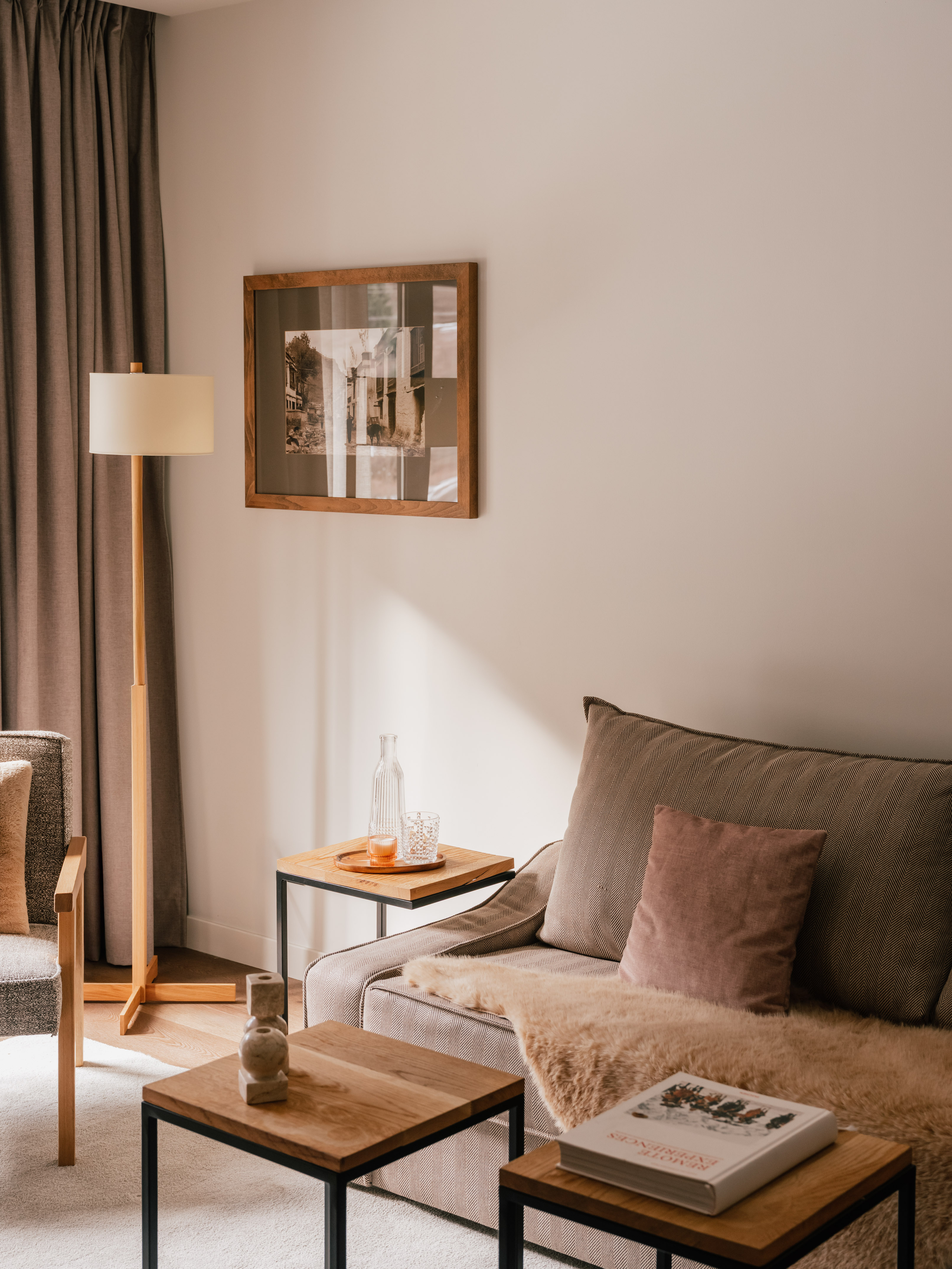 Modern living room with herringbone sofa, wooden tables, sheepskin, and art.