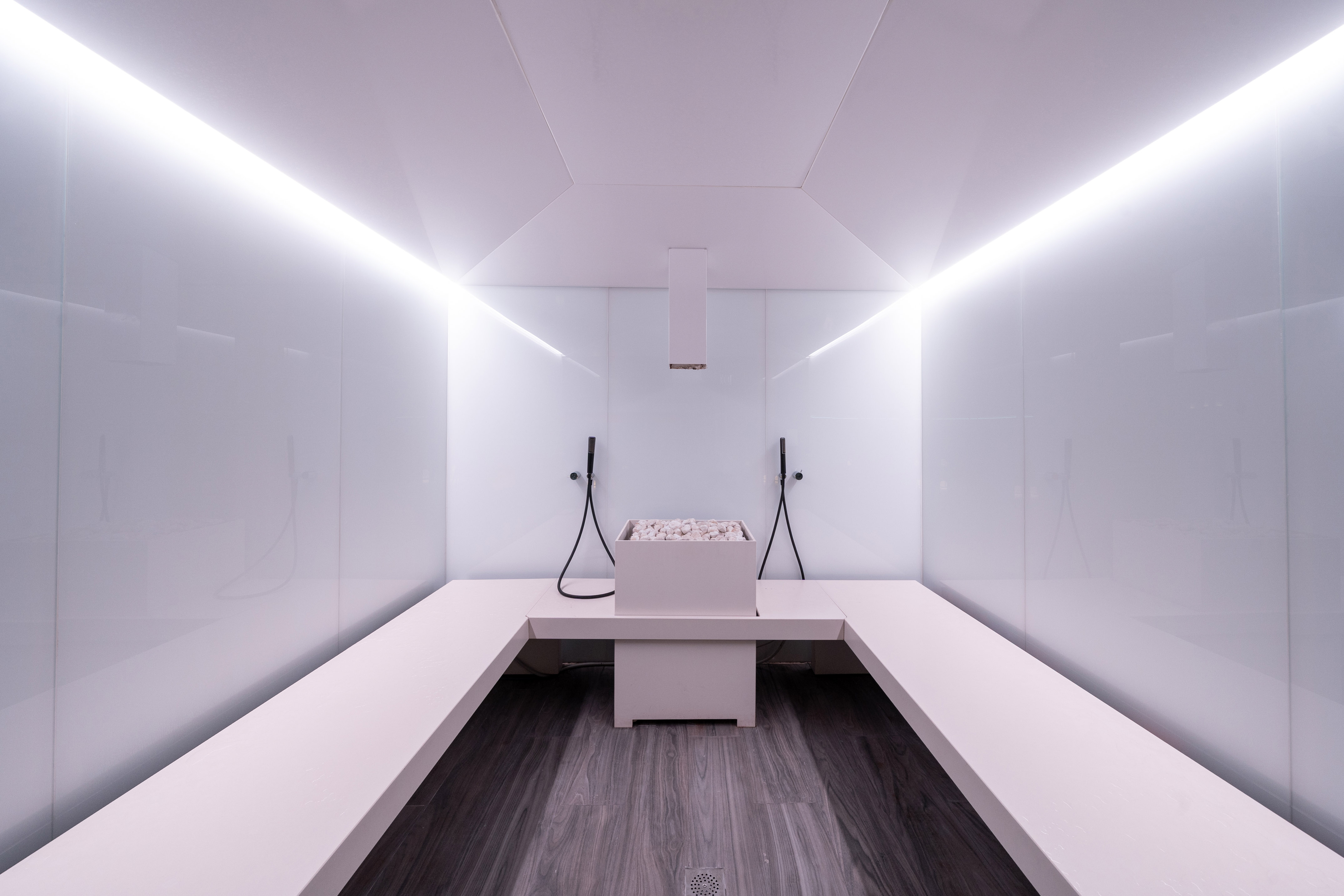 Sleek modern steam room with white benches, glowing lights, and rock heater.