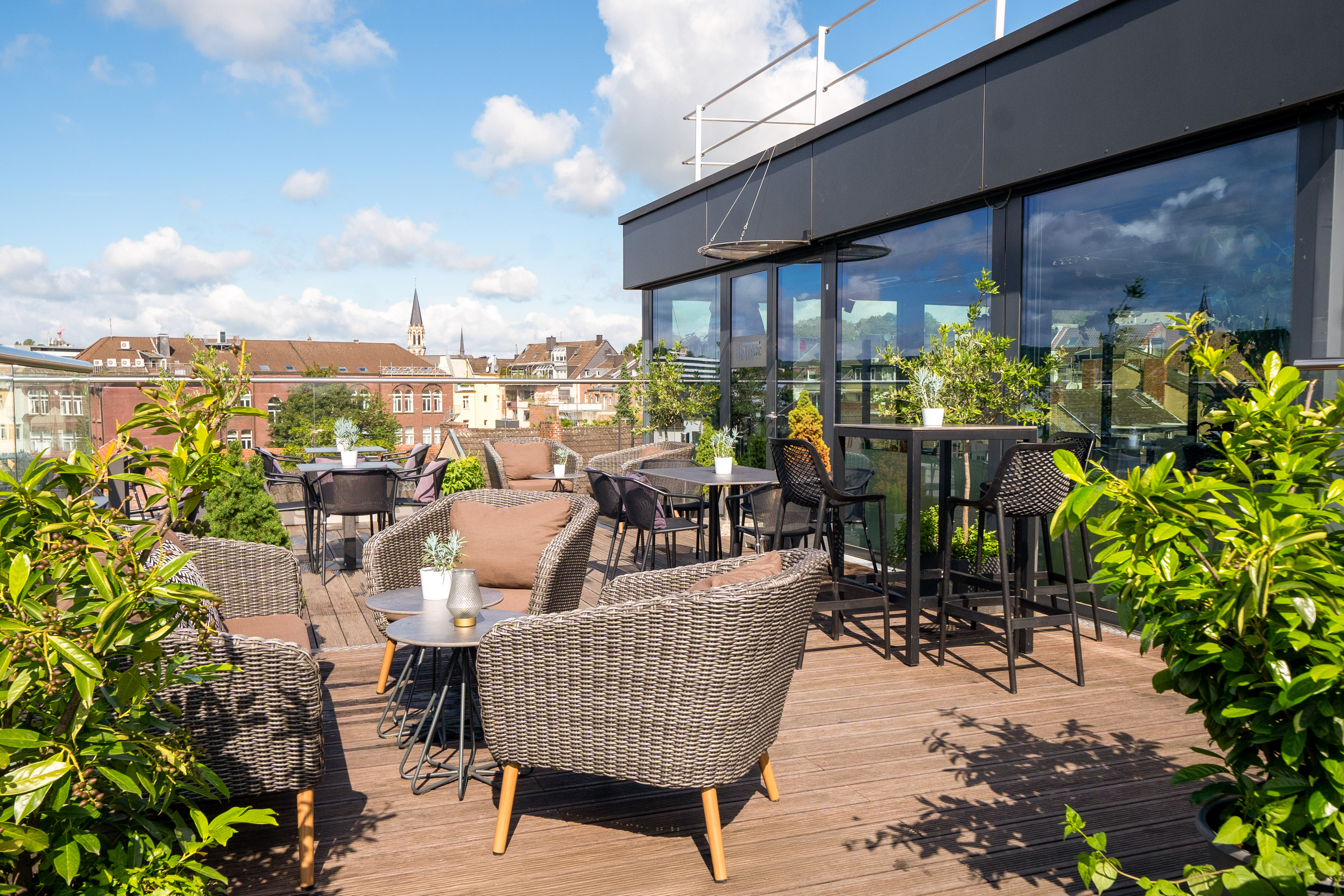 Sunny rooftop terrace with modern outdoor seating, green plants, and city views.