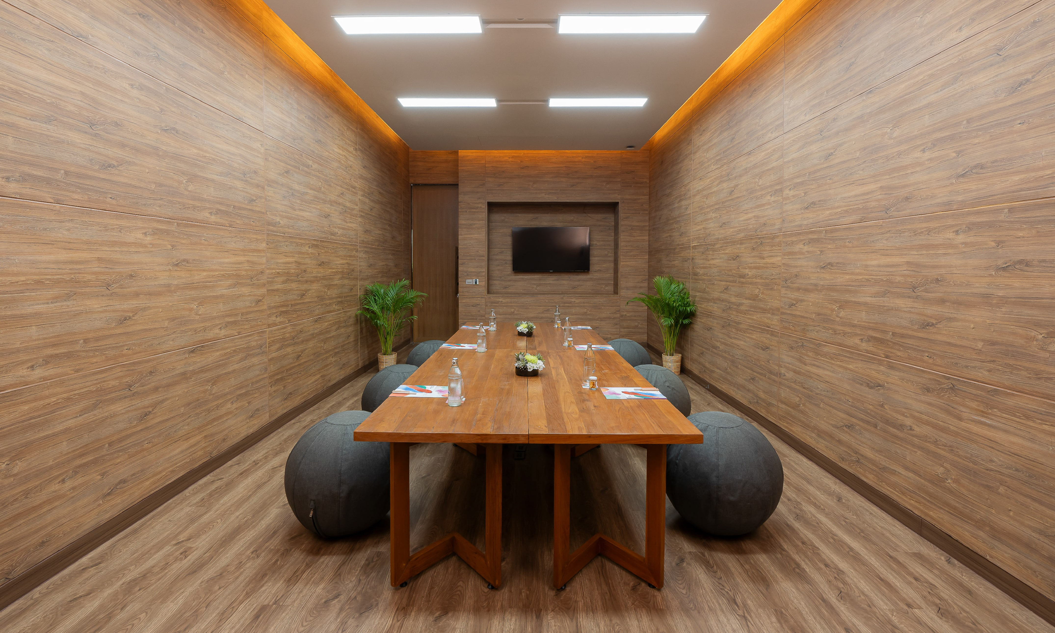 Modern wooden meeting room with long table, beanbag chairs, and TV.
