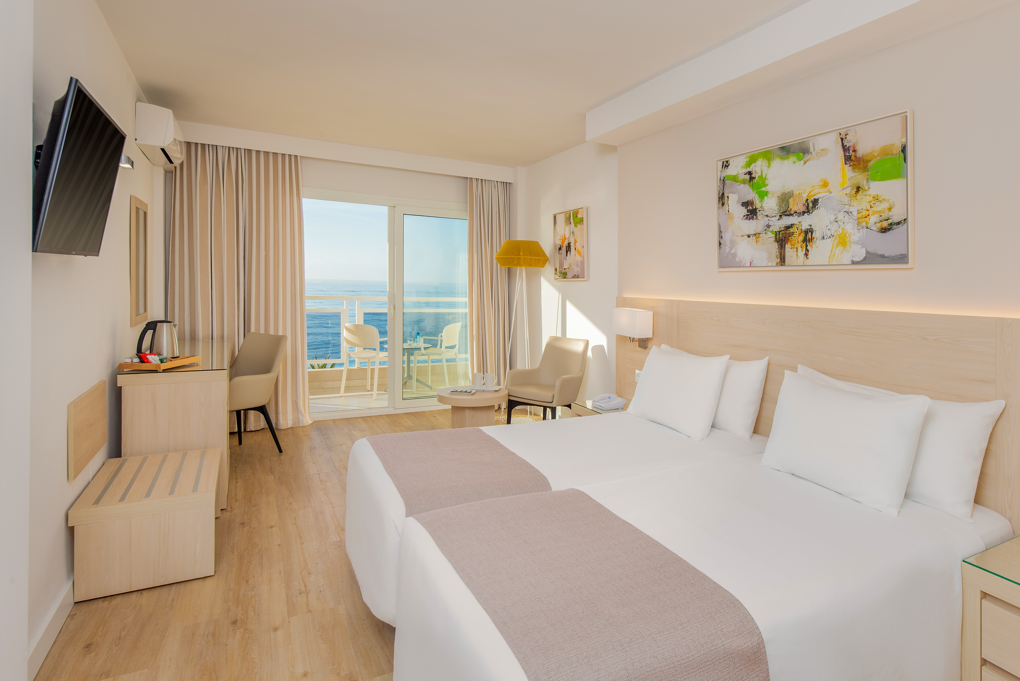 Modern hotel room with ocean view balcony, twin beds, and bright decor.