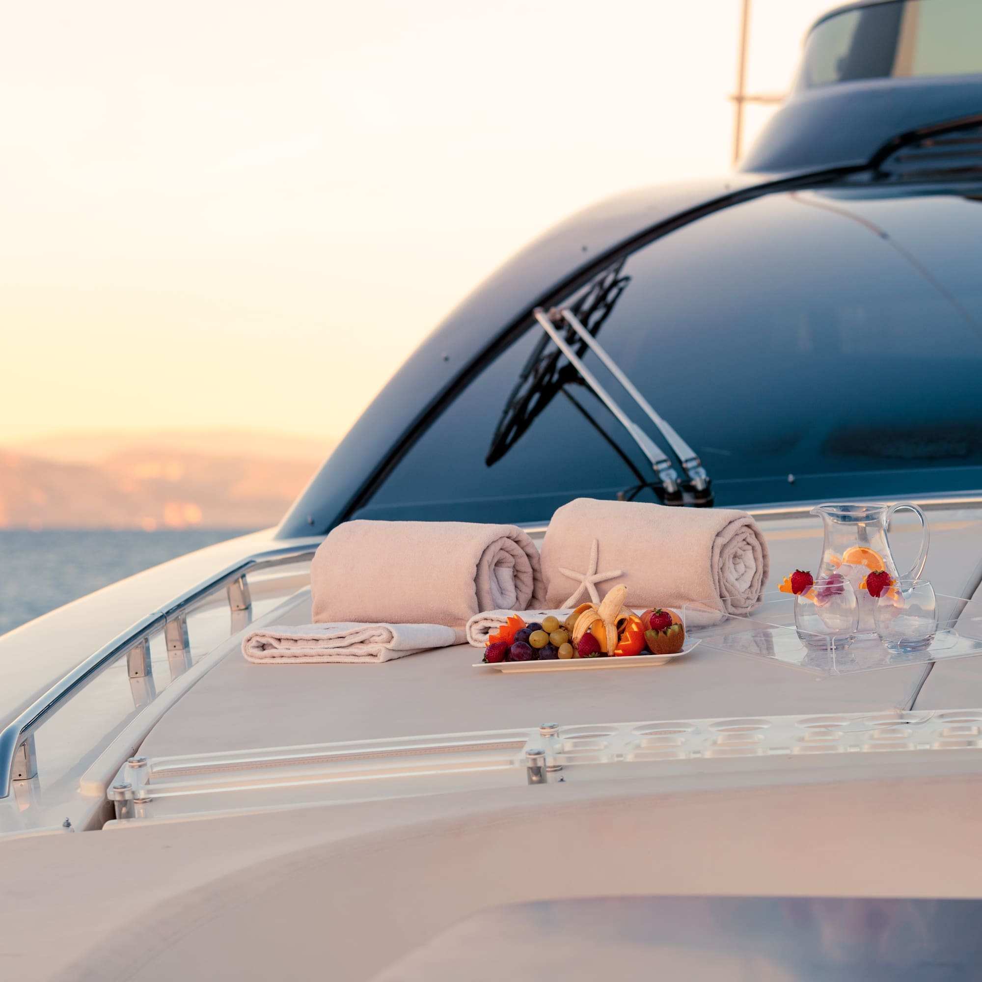 Luxury yacht deck with fresh fruit, towels, and drinks at sunset.