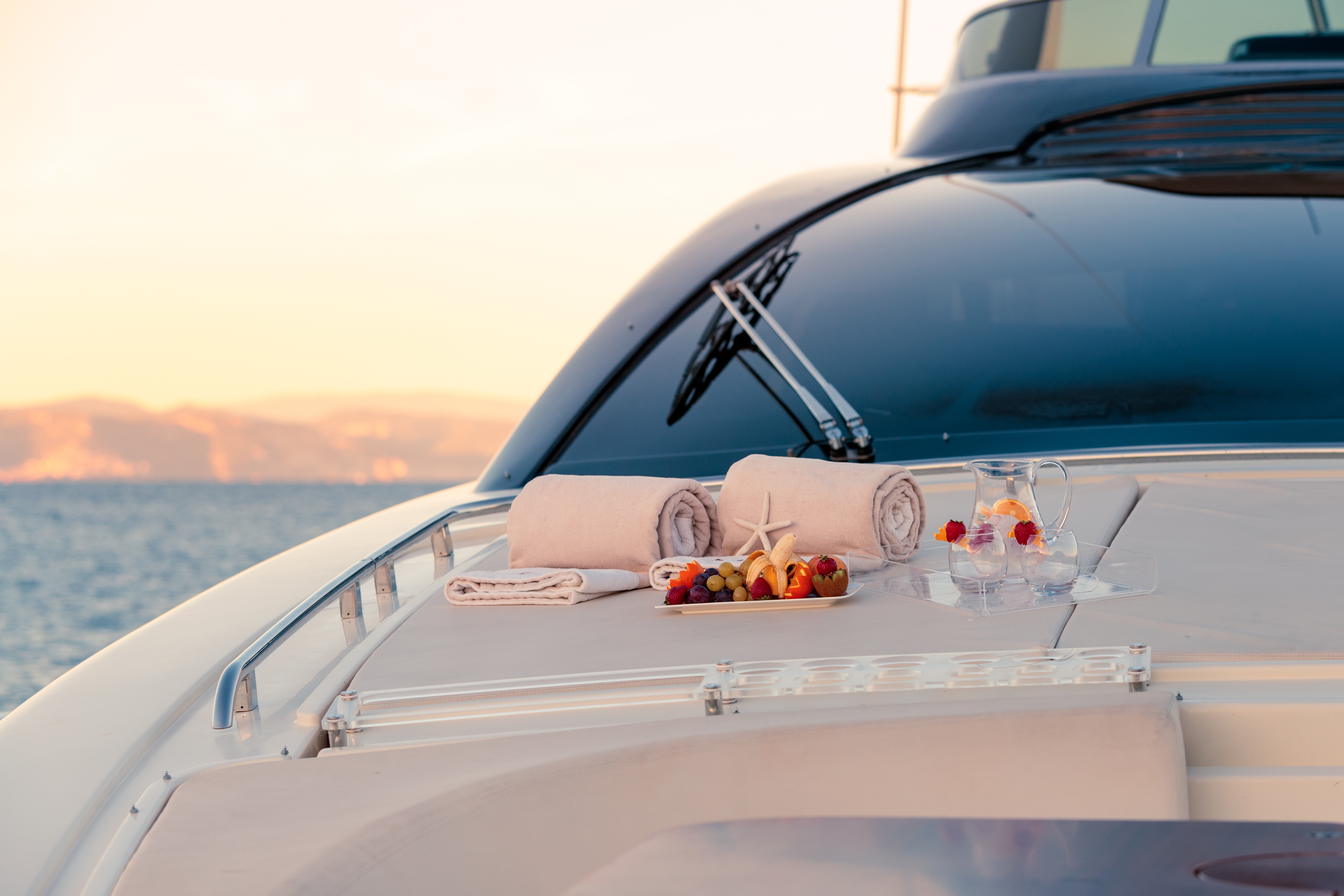 Luxury yacht deck with fresh fruit, towels, and drinks at sunset.