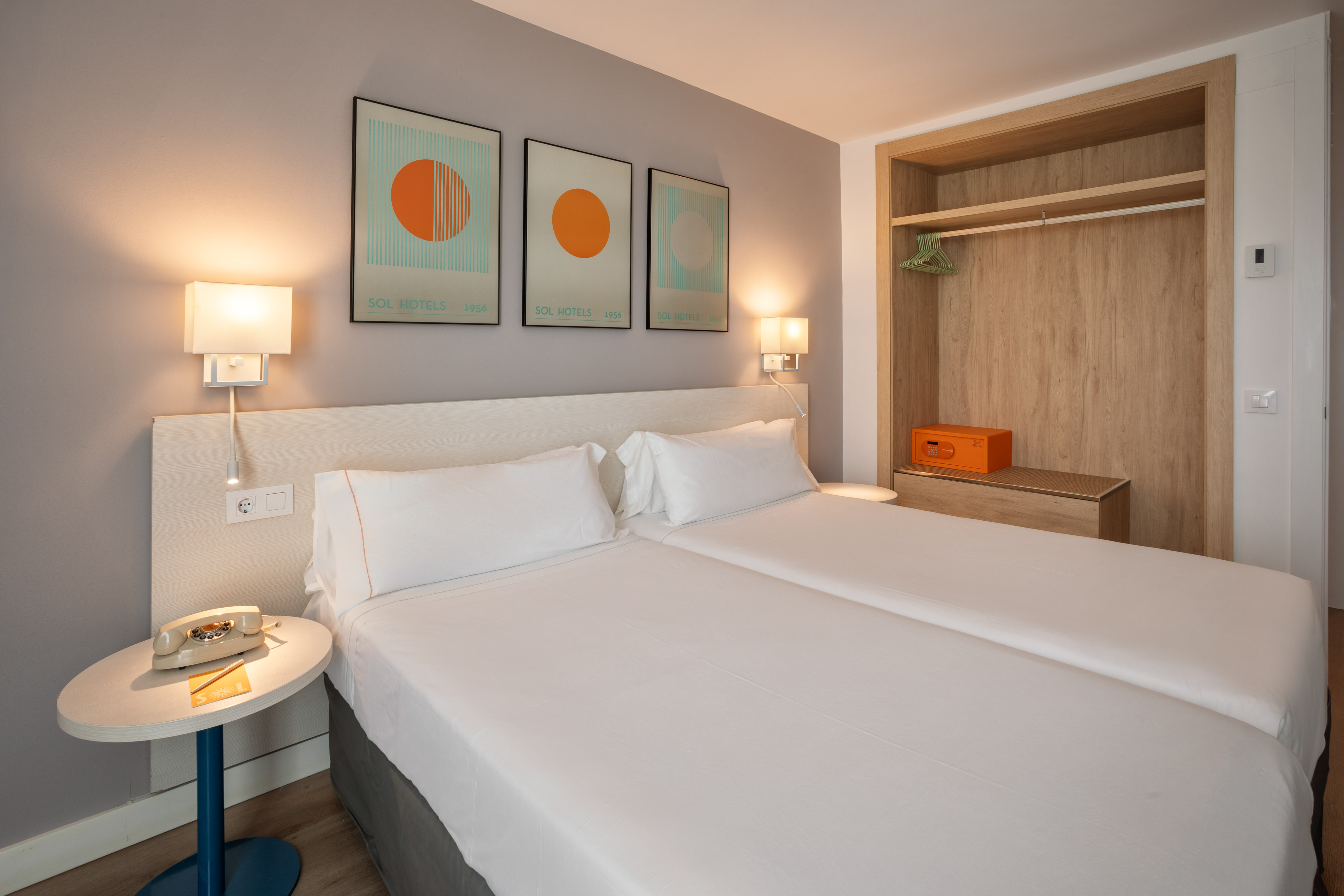 Modern hotel room with twin beds, wall art, and open wooden closet with safe.