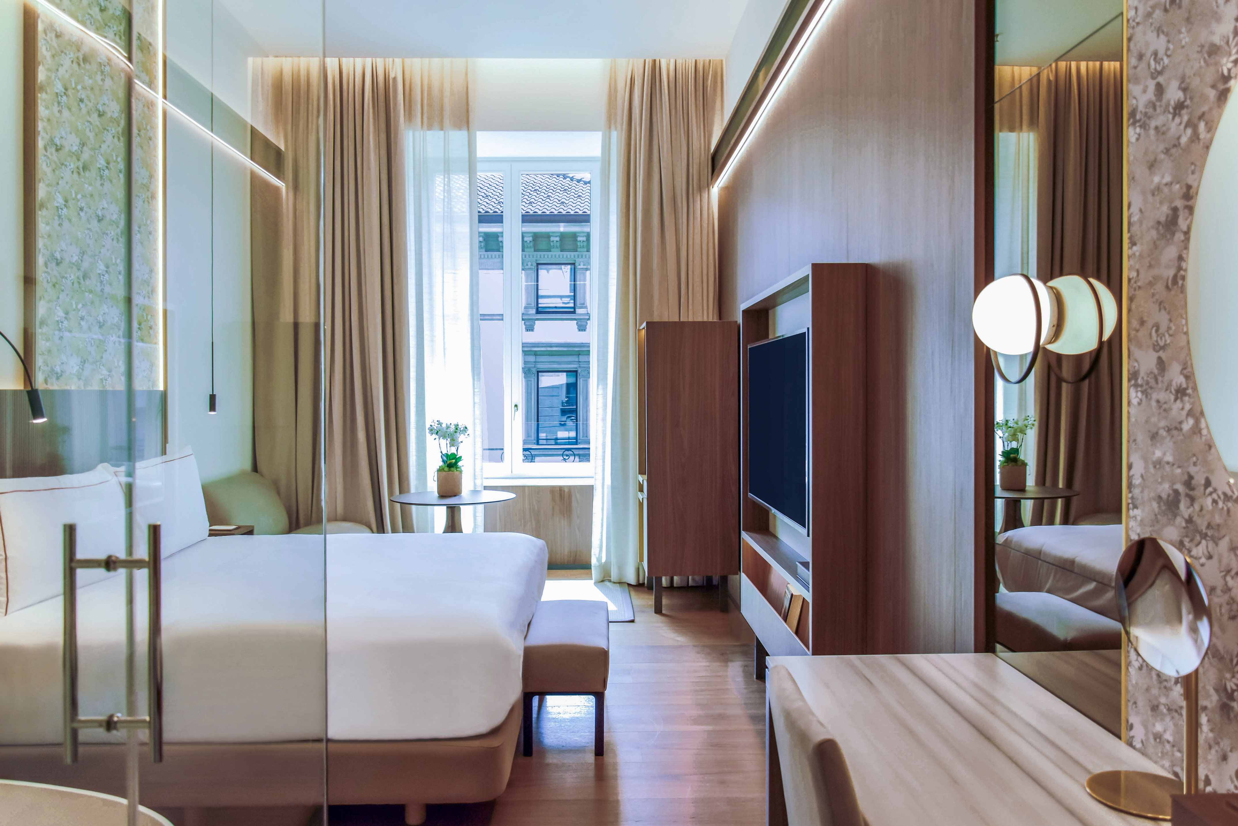 Modern hotel room with large bed, city view, wooden floor, and wall-mounted TV.