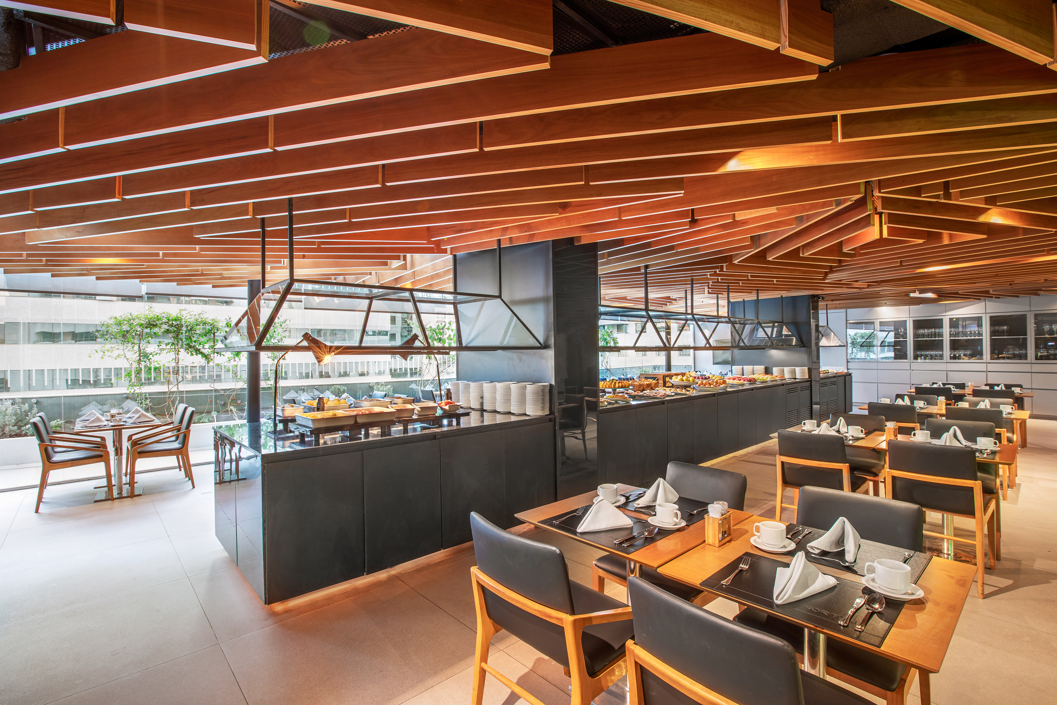 Modern restaurant buffet with wooden slat ceiling and set tables.