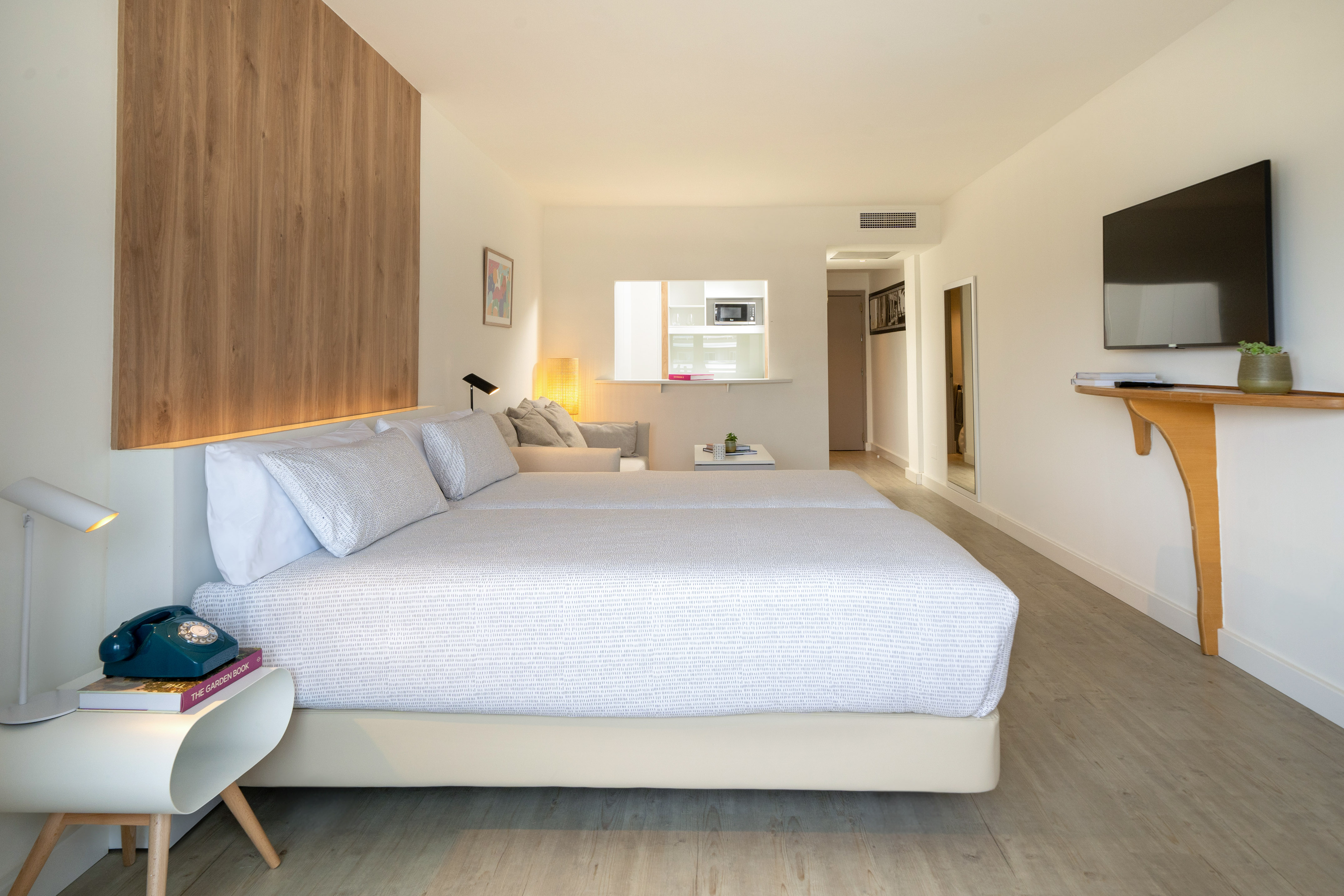Modern studio with white bed, wooden accent wall, kitchenette, and TV.