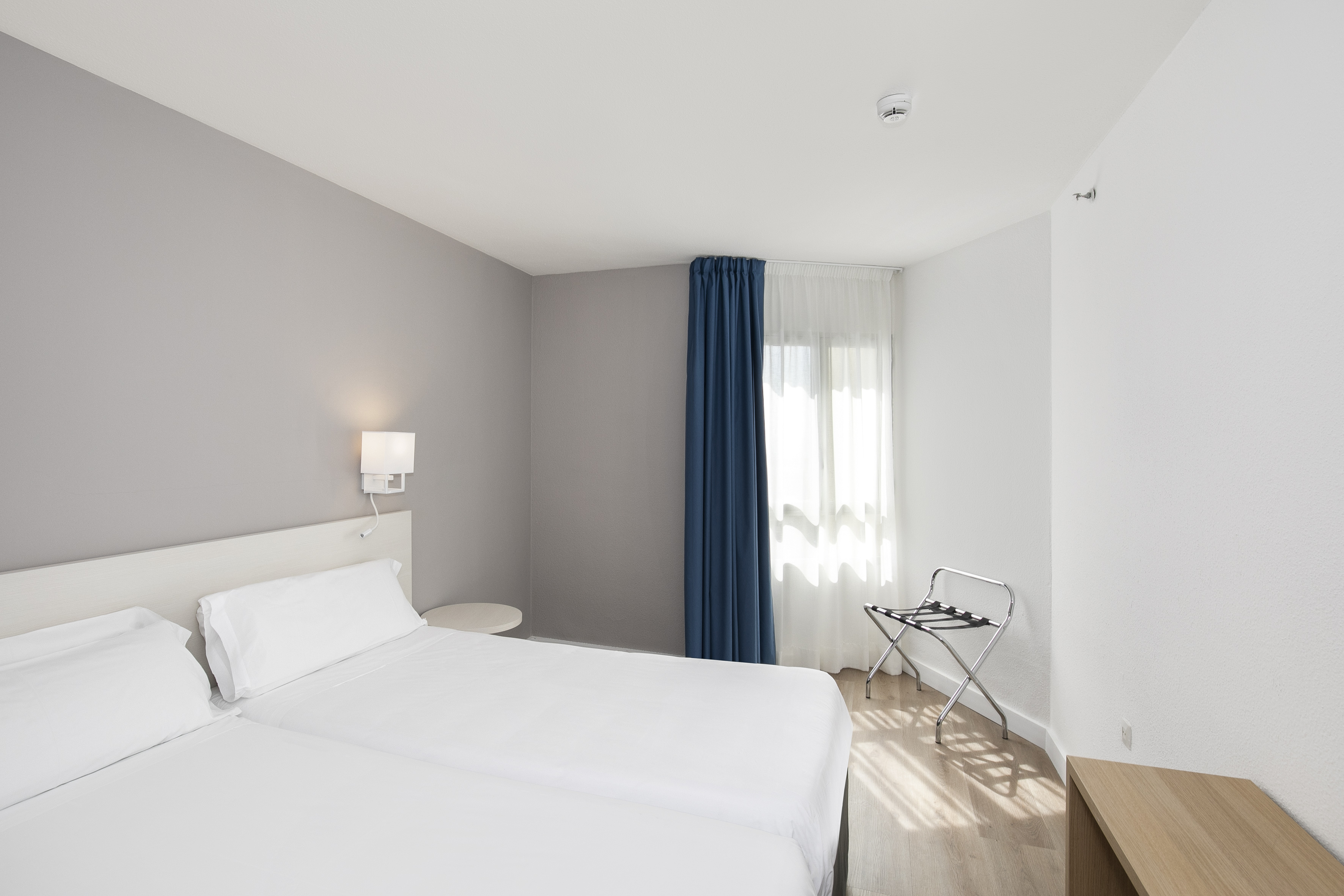 Clean modern hotel room with twin beds, blue curtains, and wooden floor.
