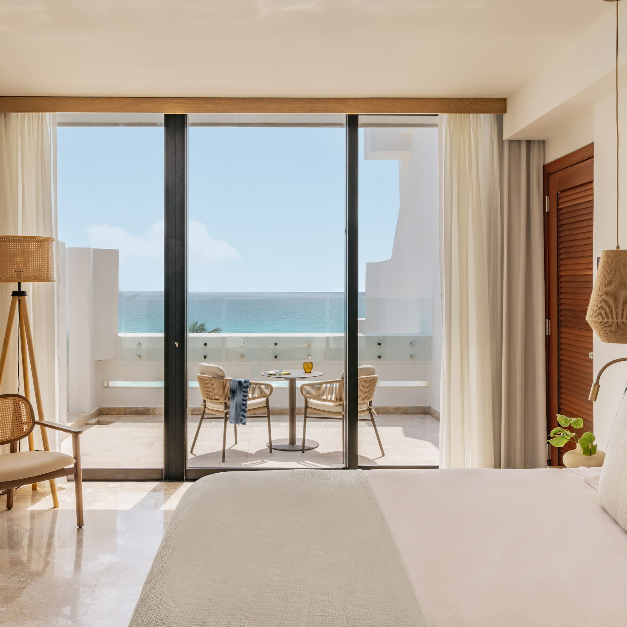 Bright coastal hotel room with oceanfront balcony and woven decor.