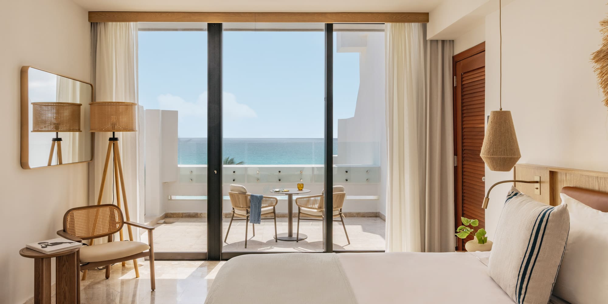 Bright coastal hotel room with oceanfront balcony and woven decor.