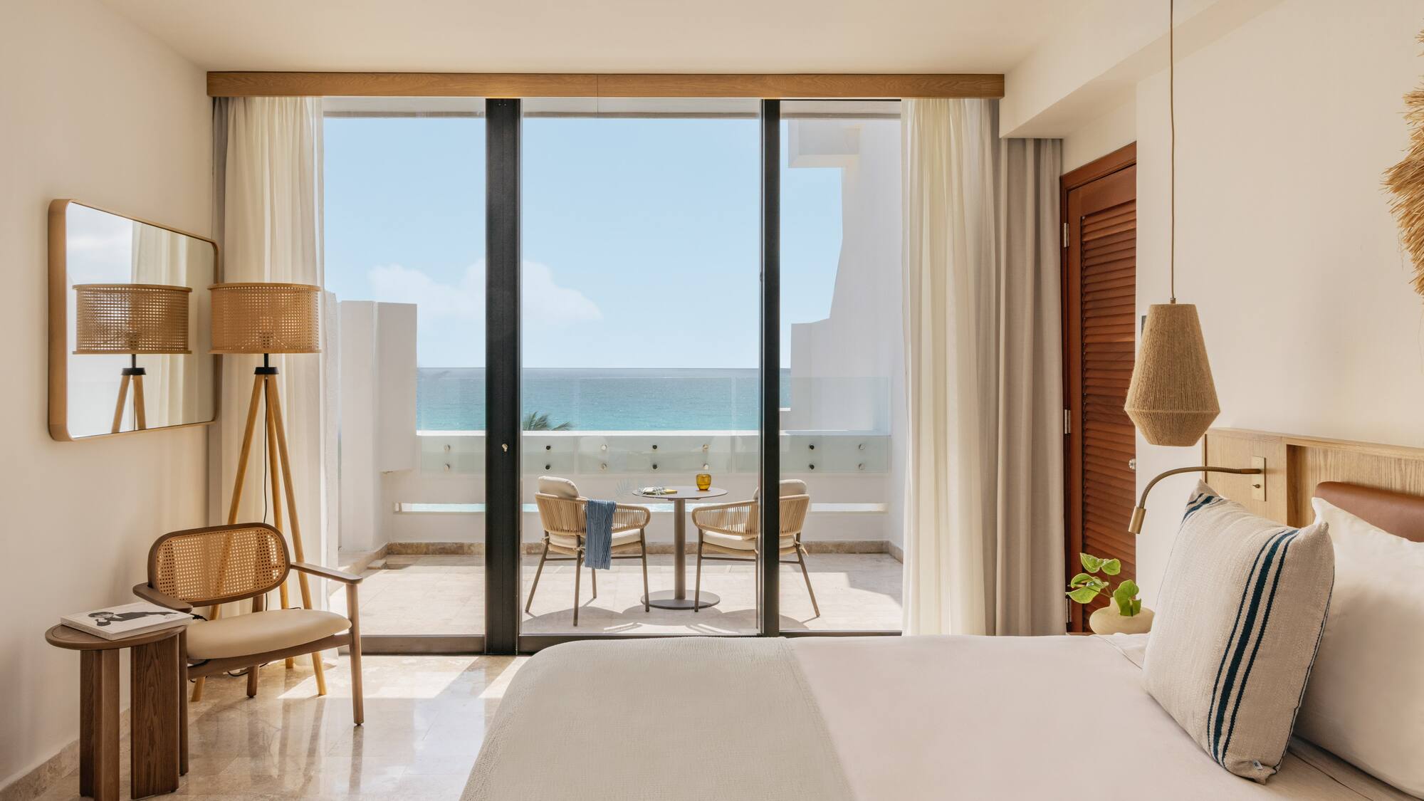 Bright coastal hotel room with oceanfront balcony and woven decor.