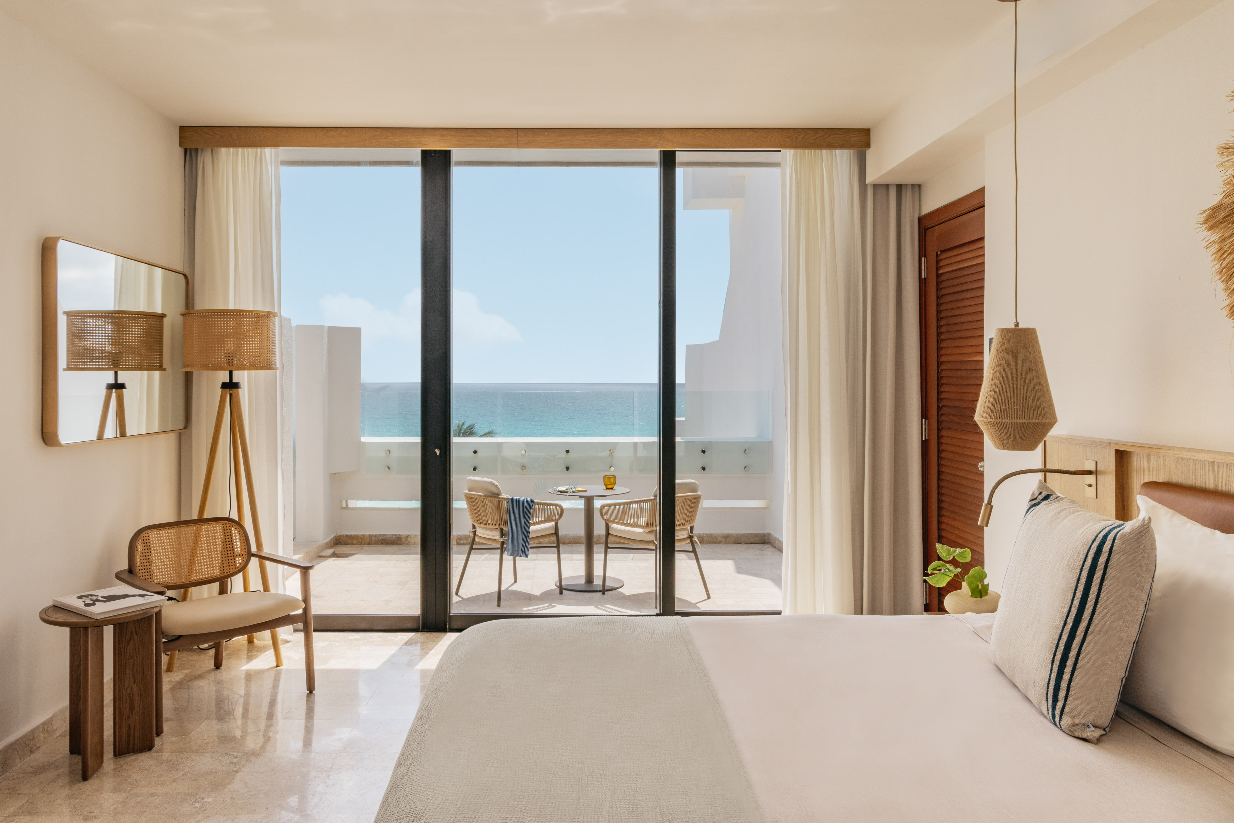 Bright coastal hotel room with oceanfront balcony and woven decor.