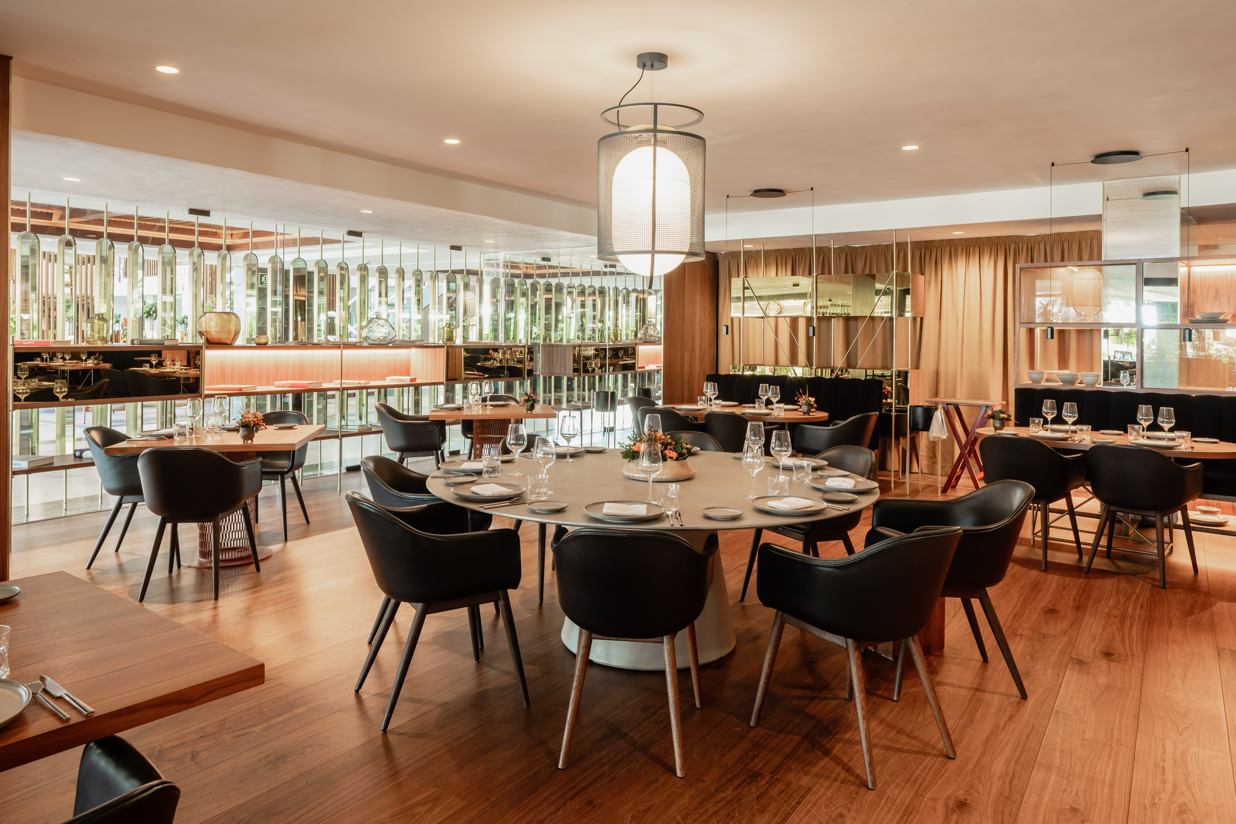 Elegant modern restaurant with set tables, black chairs, and reflective wall decor.