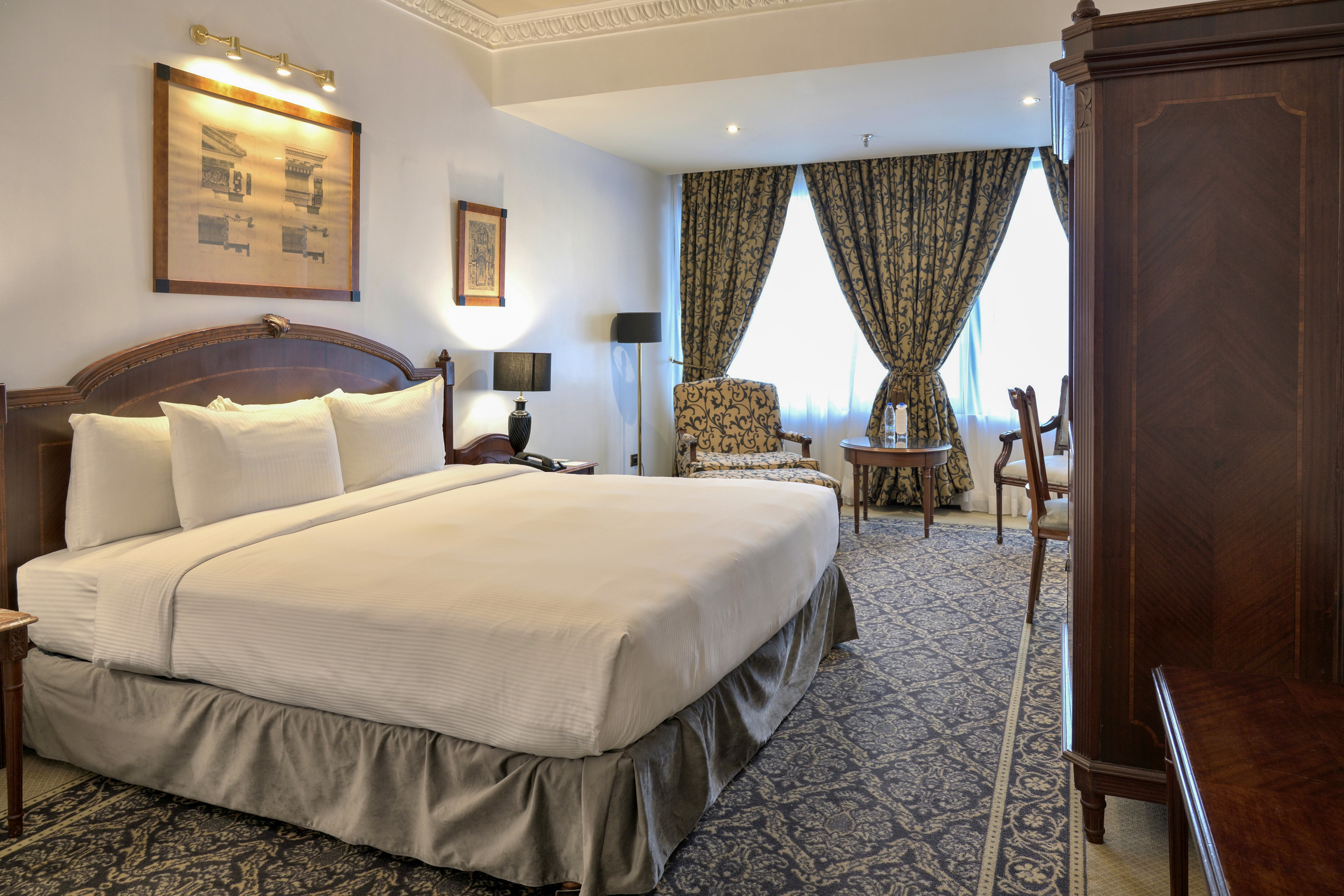 Elegant hotel bedroom with king bed, patterned rug, and classic decor.