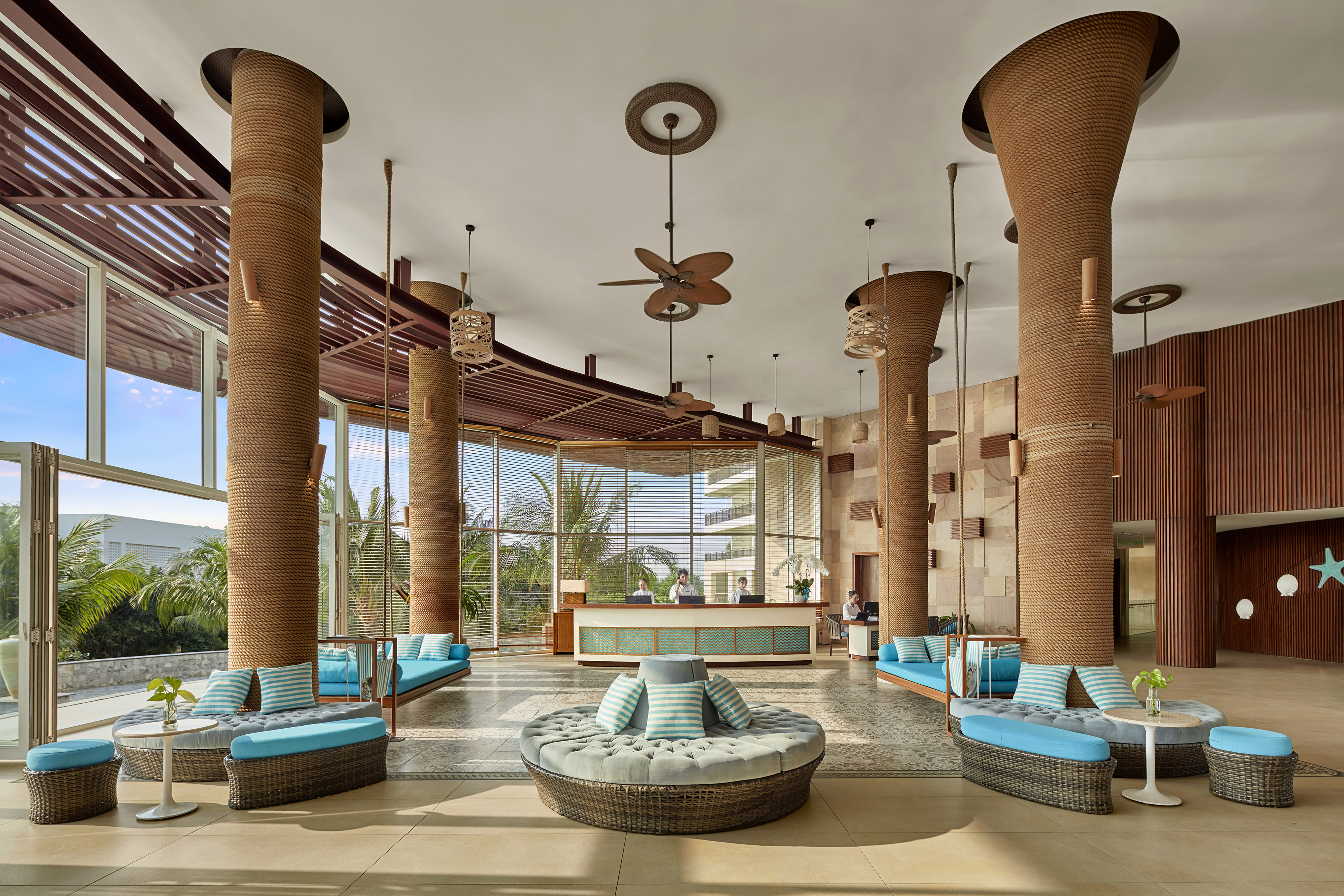 Tropical resort lobby with rope columns, rattan furniture & reception.