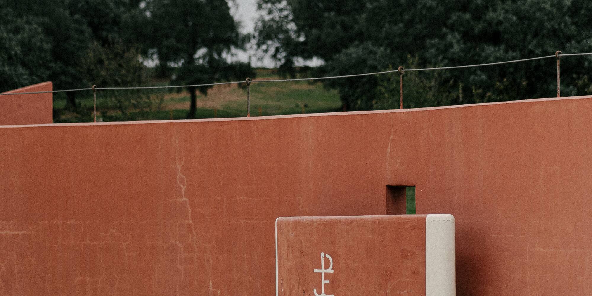 a red wall with a white square object on it with Royal Palaces of Abomey in the background