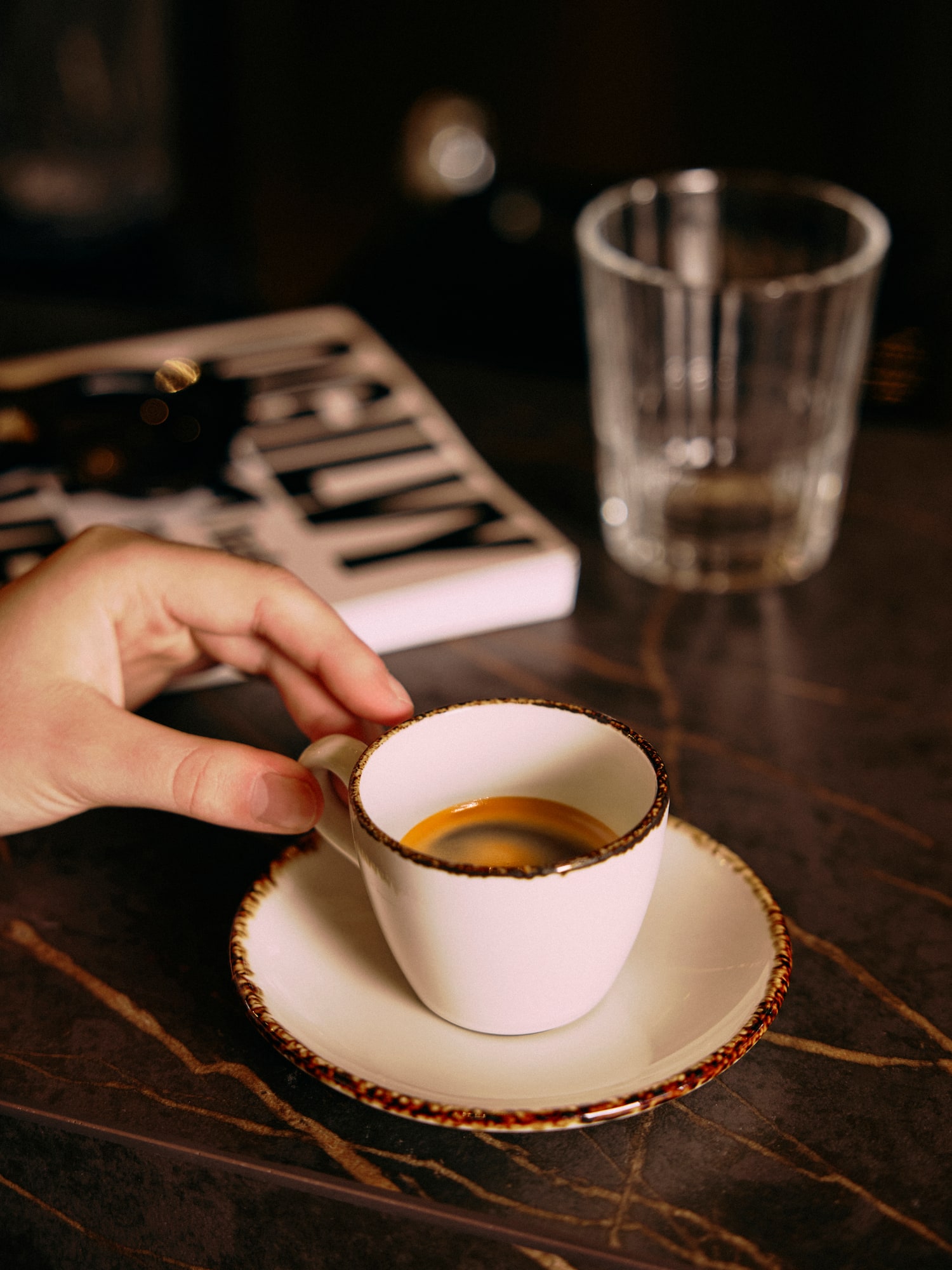 Mano sosteniendo taza blanca de espresso con crema en mesa oscura.