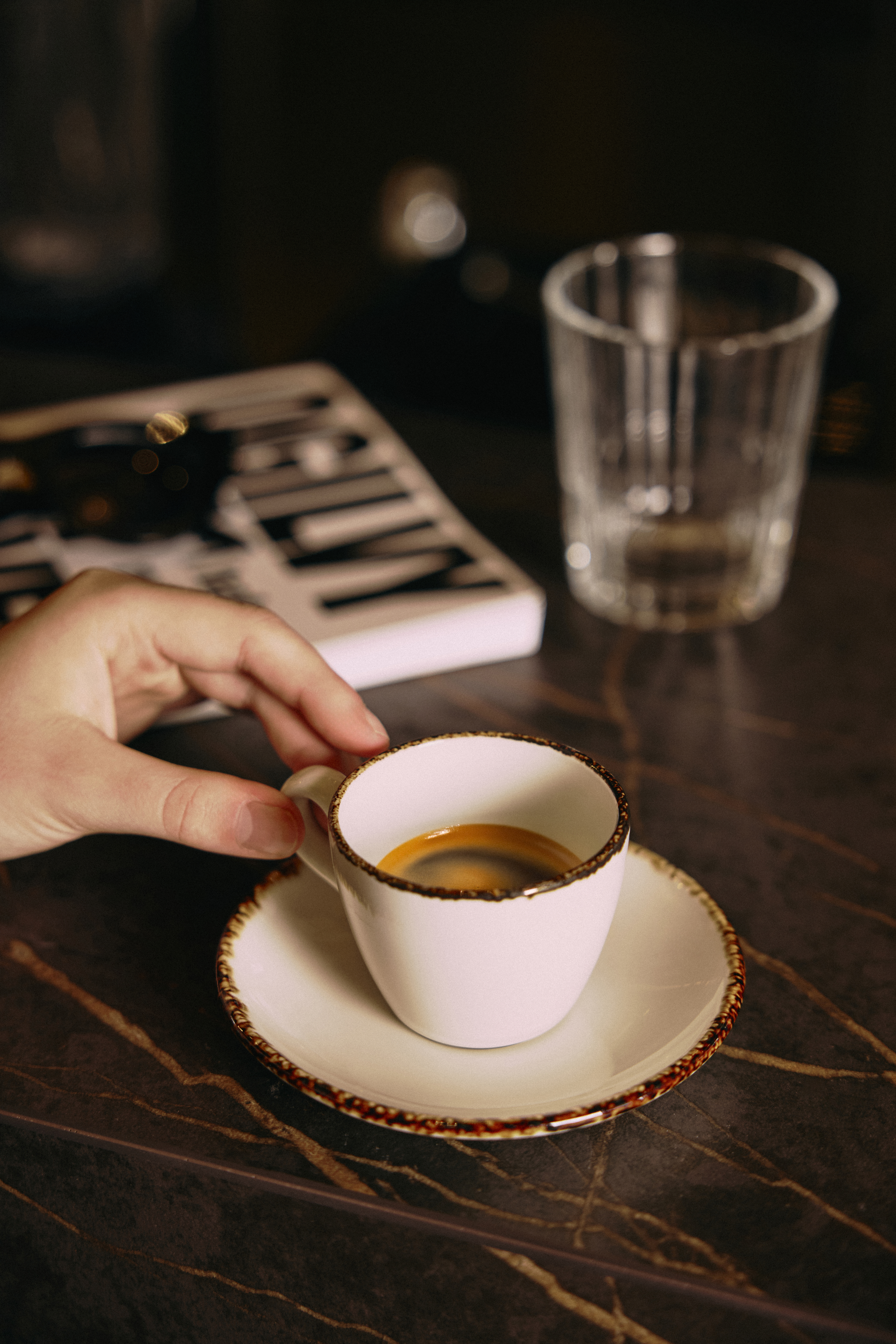 Mano sosteniendo taza blanca de espresso con crema en mesa oscura.
