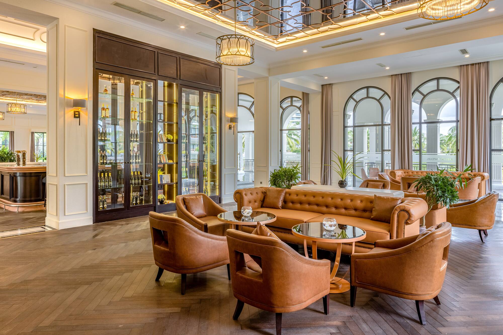 Elegant hotel lounge with leather seating, display bar, and arched windows.