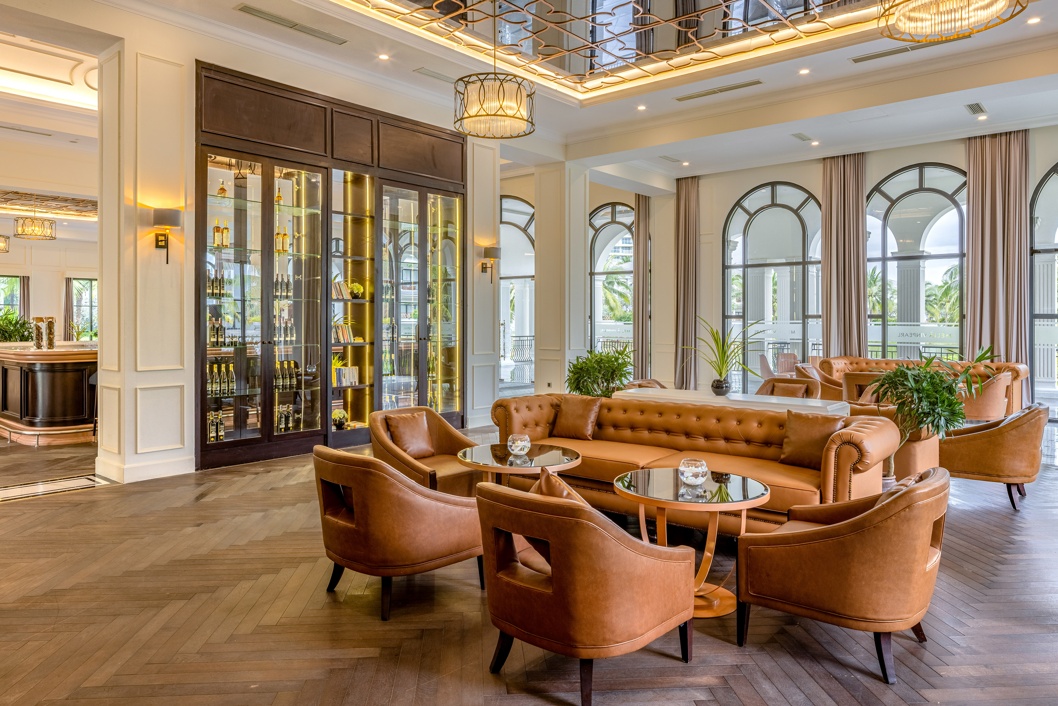 Elegant hotel lounge with leather seating, display bar, and arched windows.