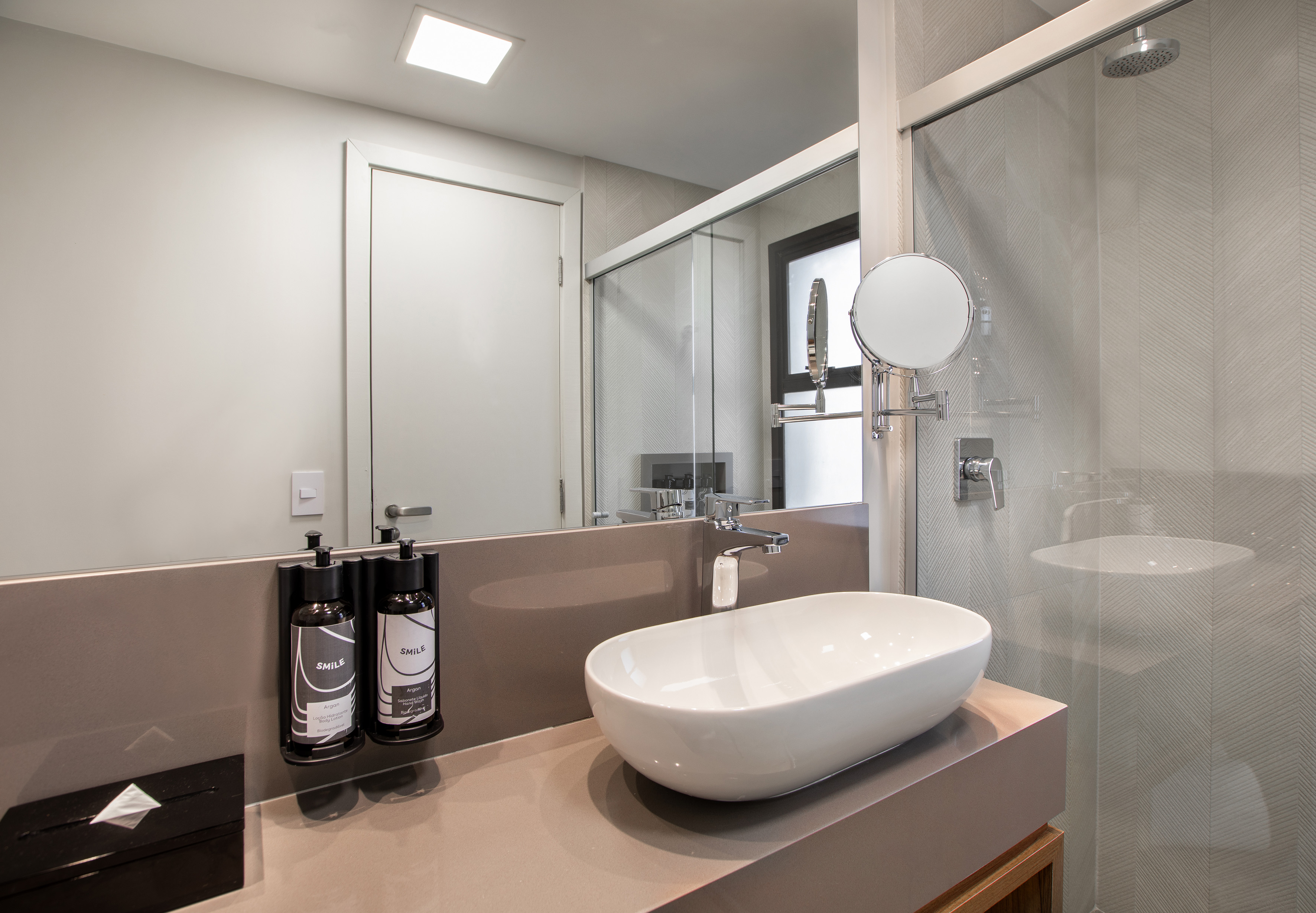 Modern hotel bathroom vanity with vessel sink, mirror, chrome faucet, and glass shower.