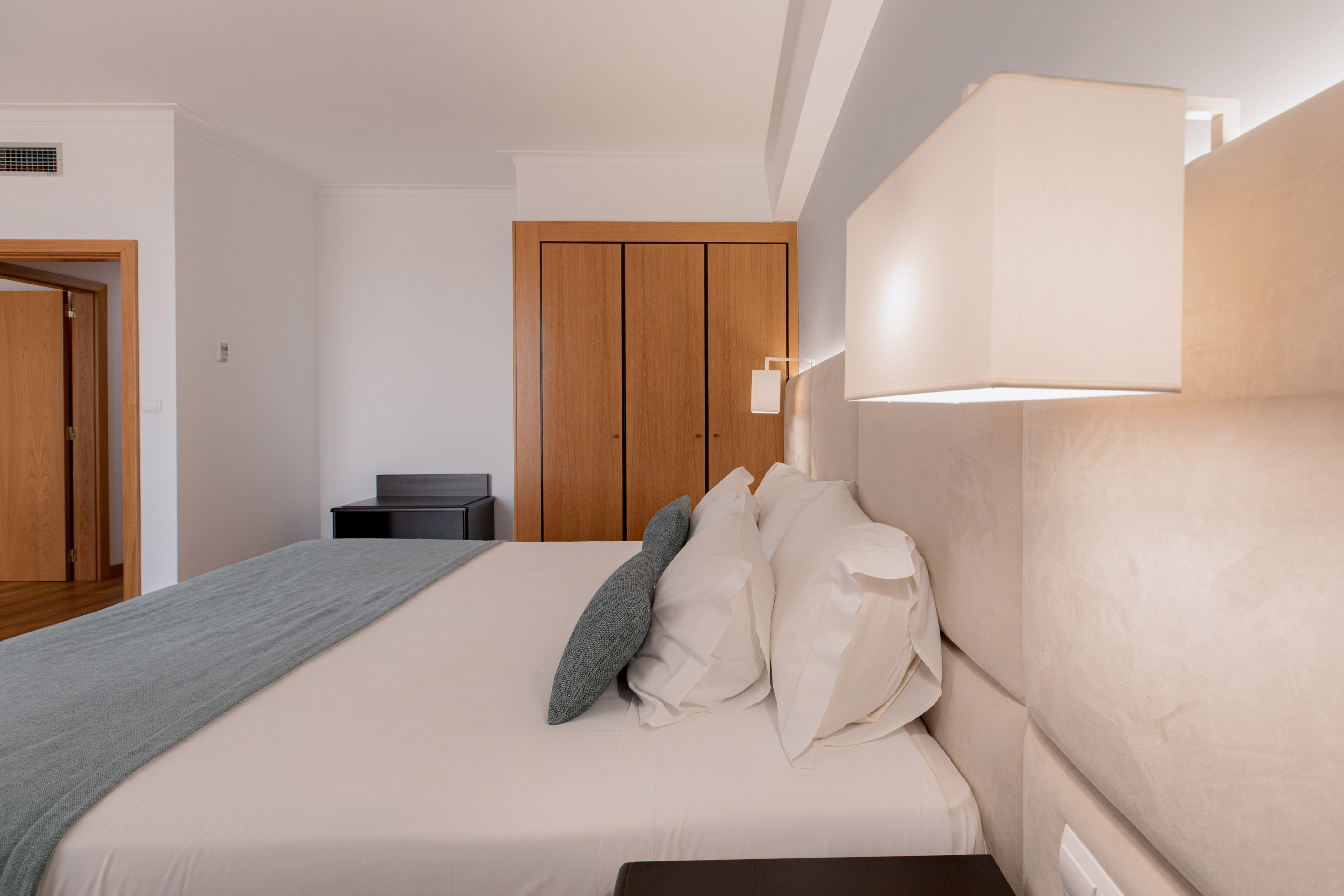 Modern hotel bedroom with large bed, white linens, blue throw, and wooden wardrobe.