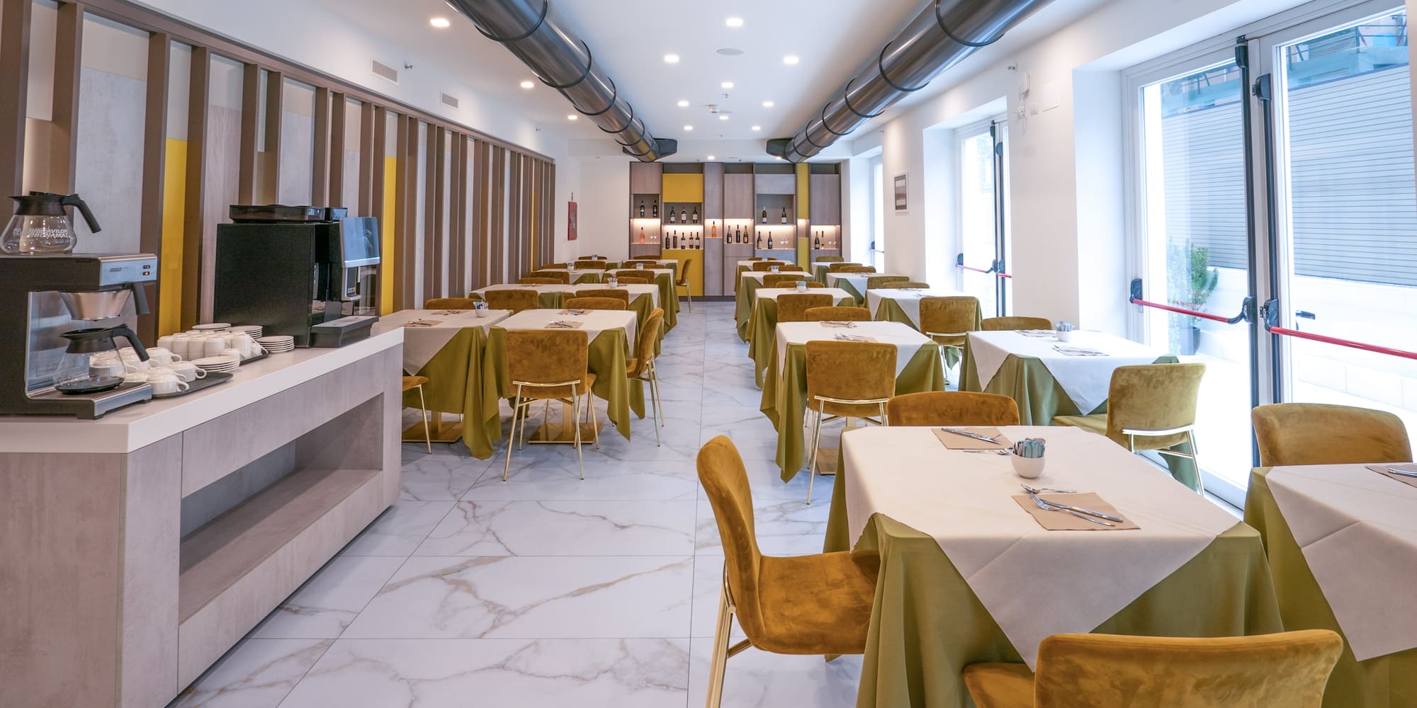 Modern hotel dining room with gold chairs, olive tables, and coffee buffet.