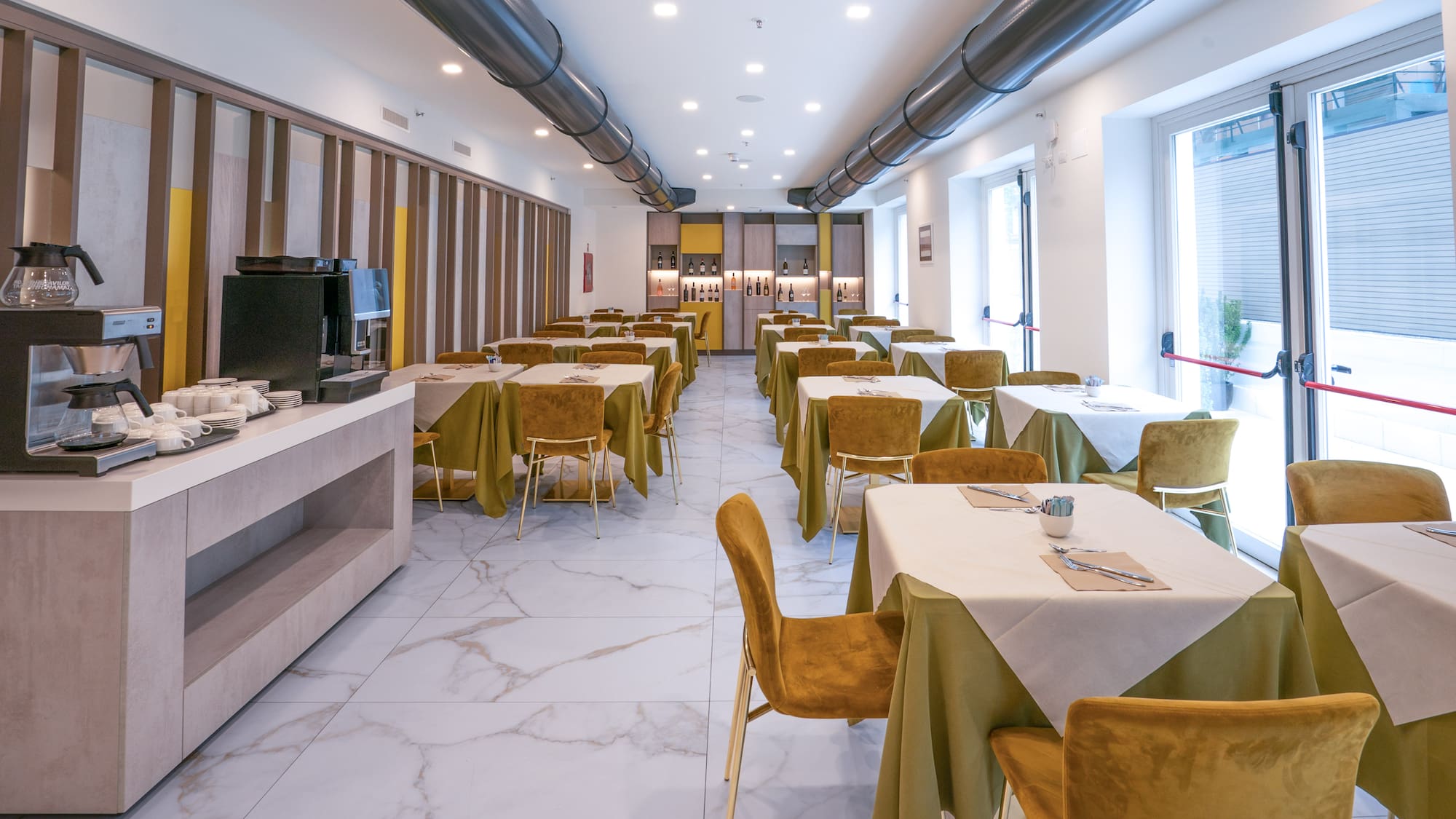 Hotel dining room with set tables, gold chairs, green linens, and coffee buffet.