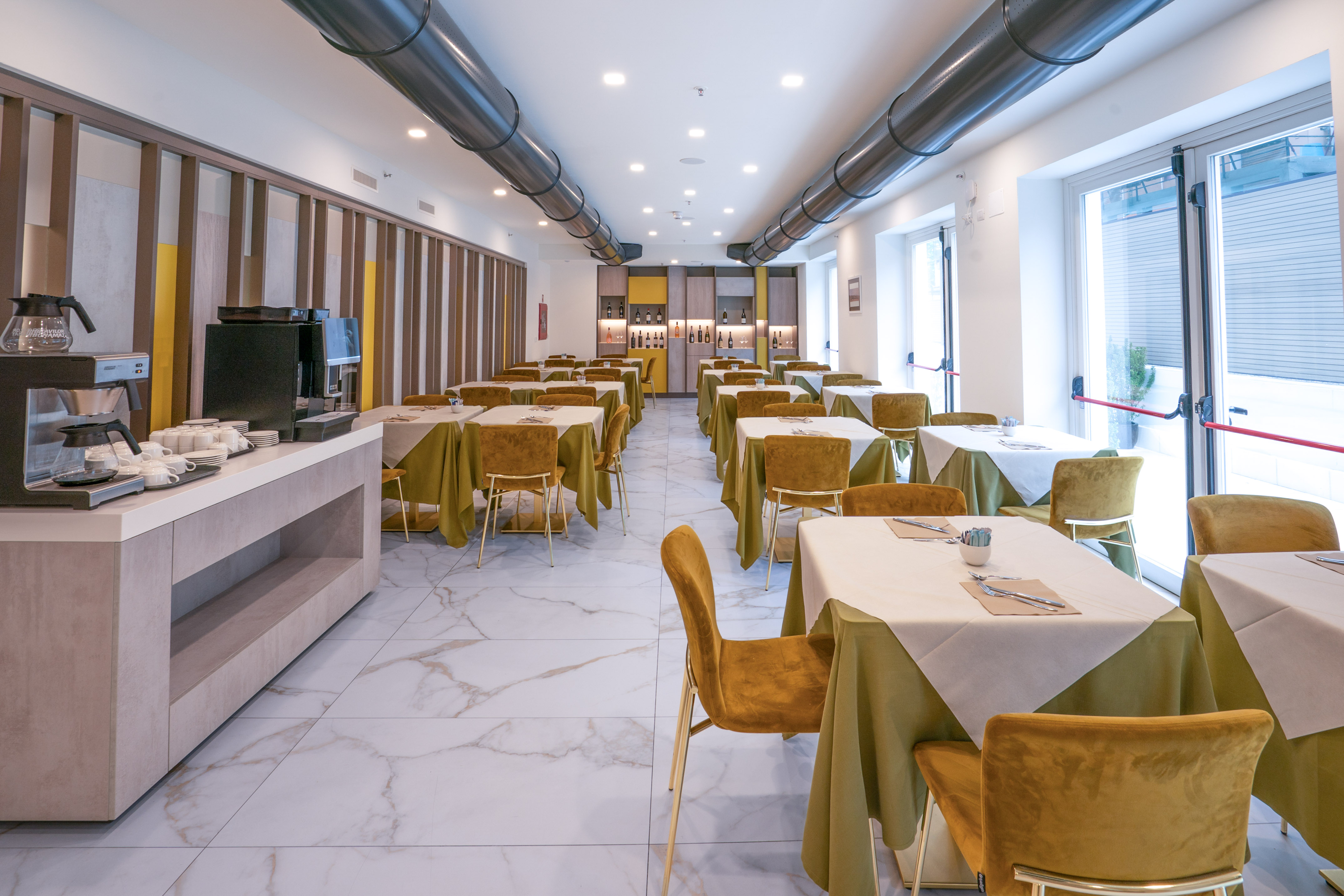Hotel dining room with set tables, gold chairs, green linens, and coffee buffet.