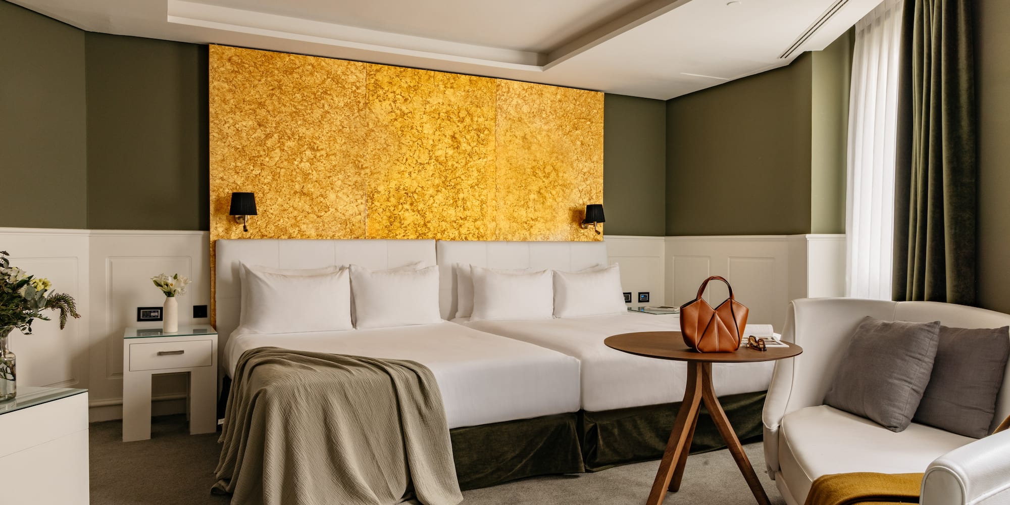 Habitación hotel de lujo con camas dobles, cabecero dorado y decoración verde oliva.