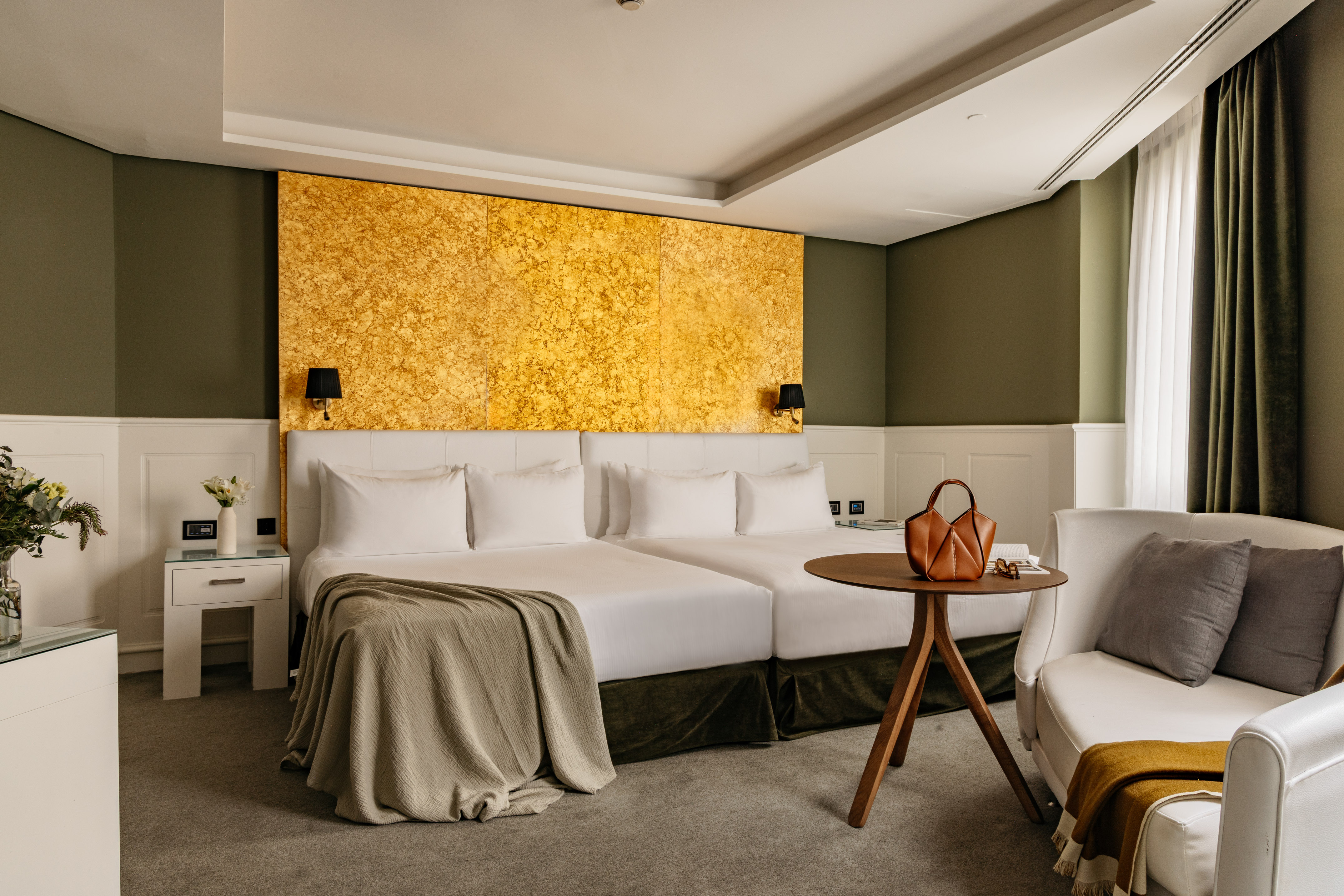 Habitación hotel de lujo con camas dobles, cabecero dorado y decoración verde oliva.