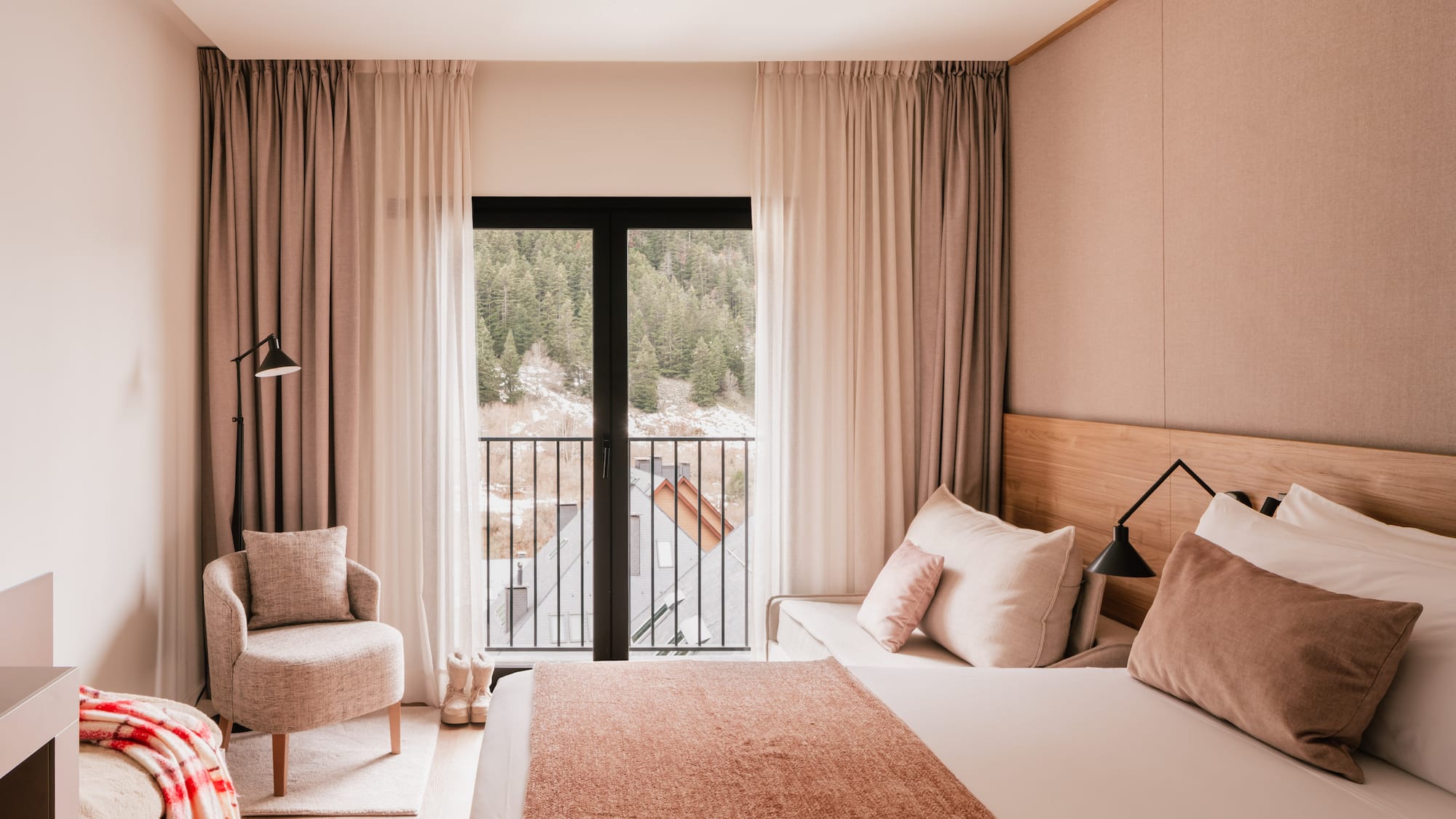 Modern hotel bedroom with mountain view balcony, cozy armchair, and neutral decor.