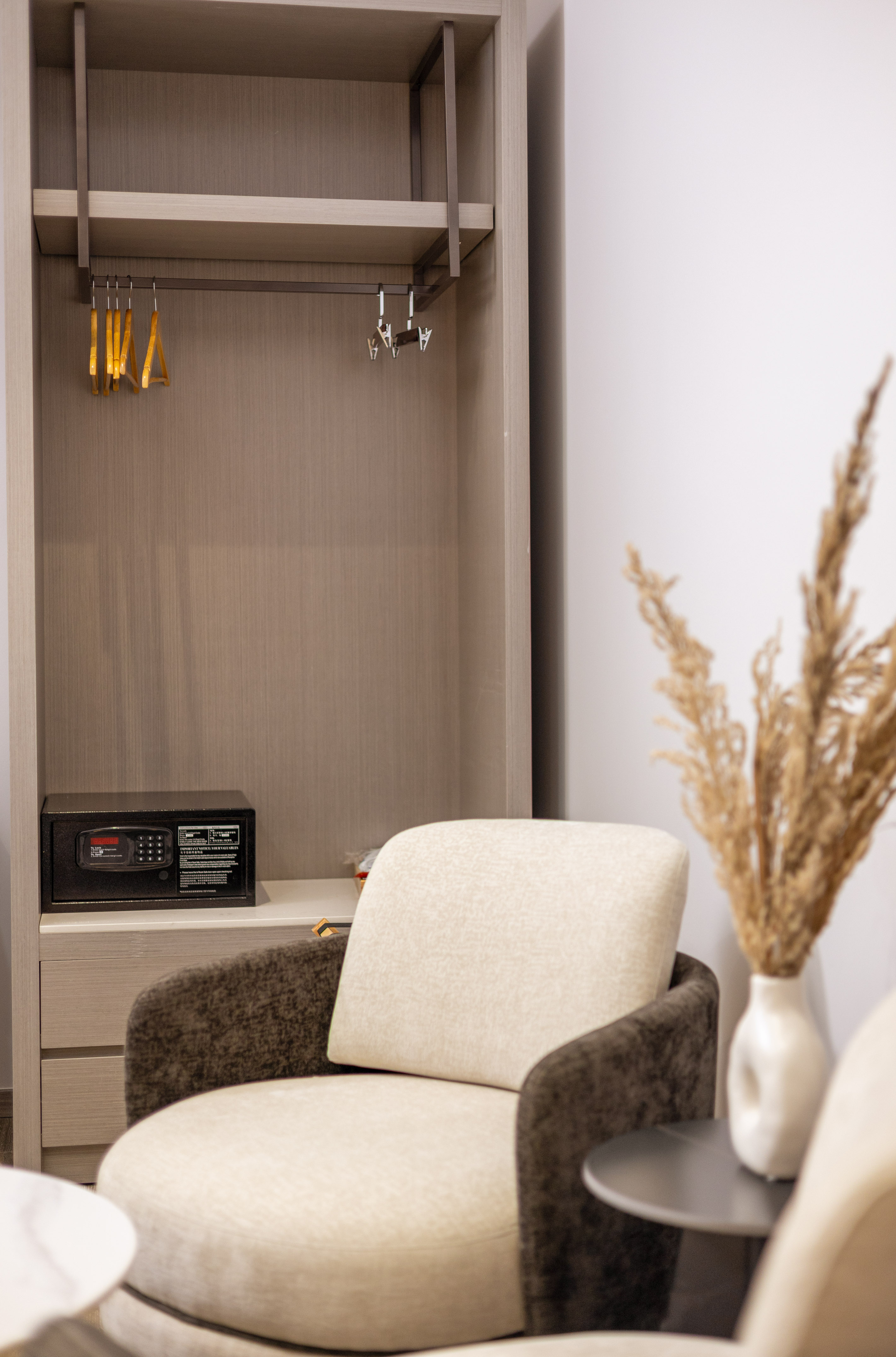 Hotel room wardrobe with safe, hangers, and comfortable beige armchair.