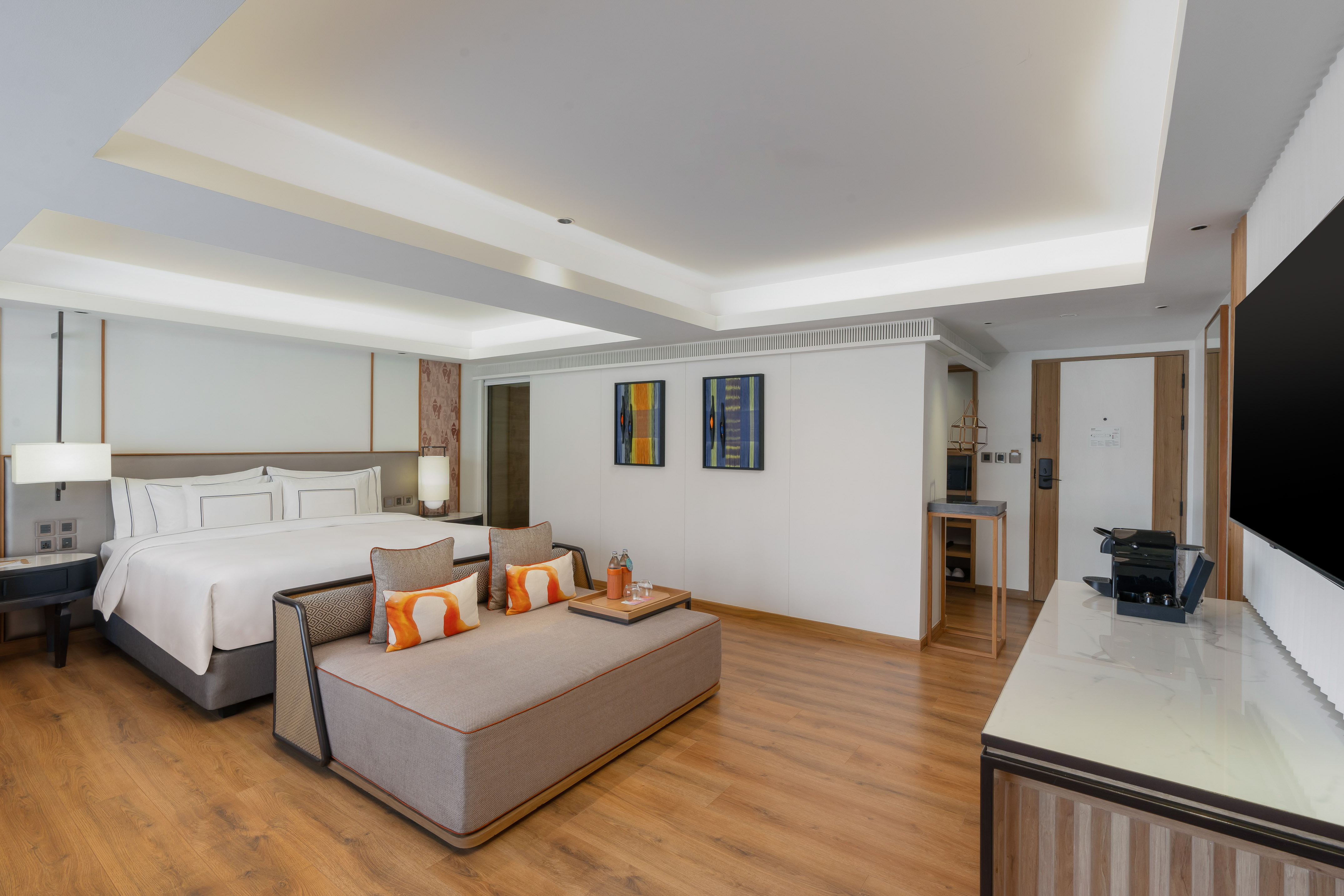 Stylish hotel suite featuring king bed, daybed, abstract art, and hardwood floor.