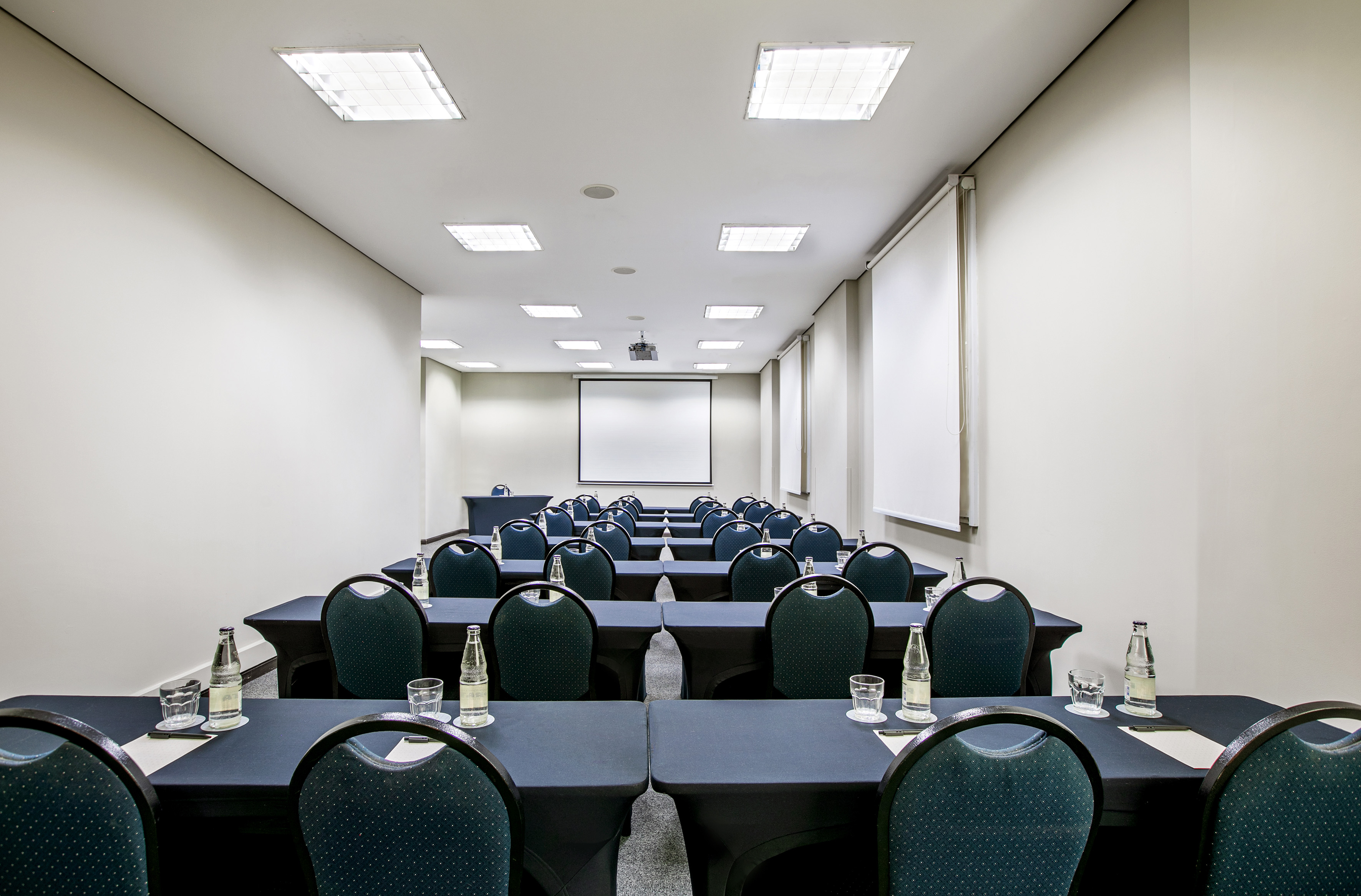 Empty conference room with projector screen, dark tables, and chairs.
