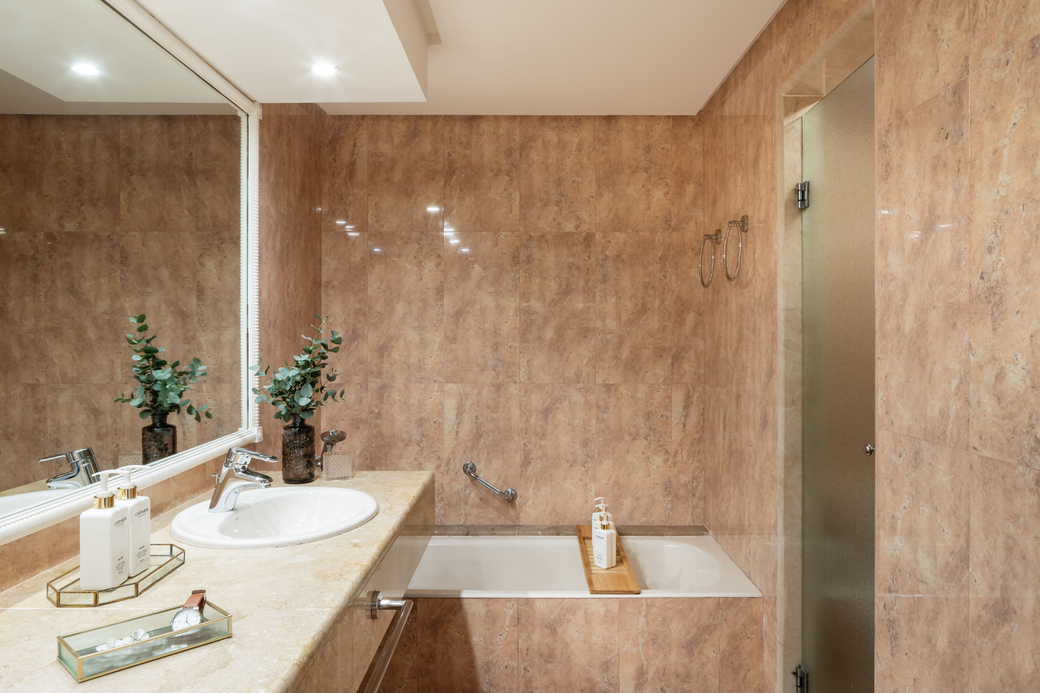 Beige marble bathroom with vanity sink, mirror, bathtub, and frosted glass shower.