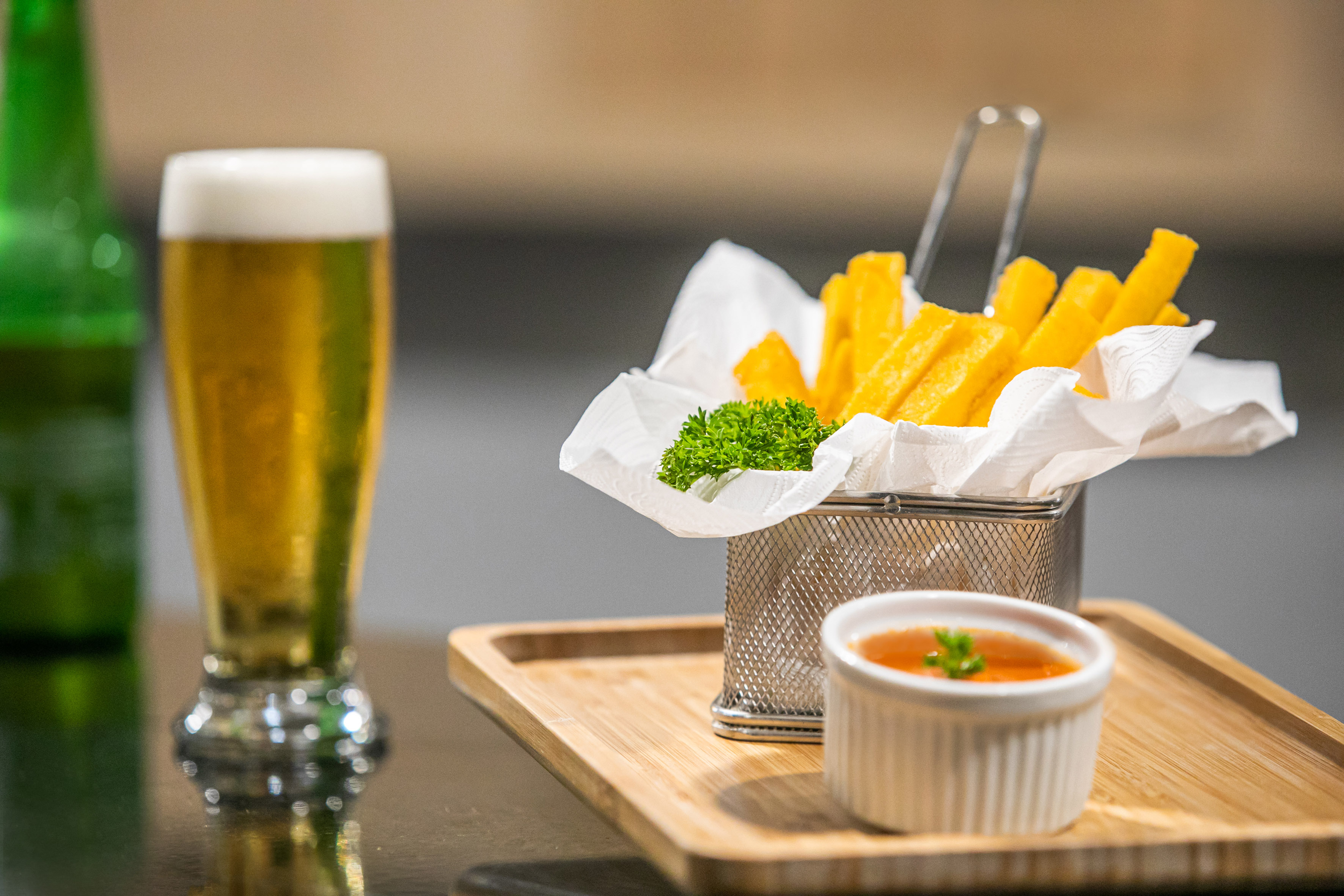 Golden beer, polenta fries with parsley, and dipping sauce on a wooden tray.