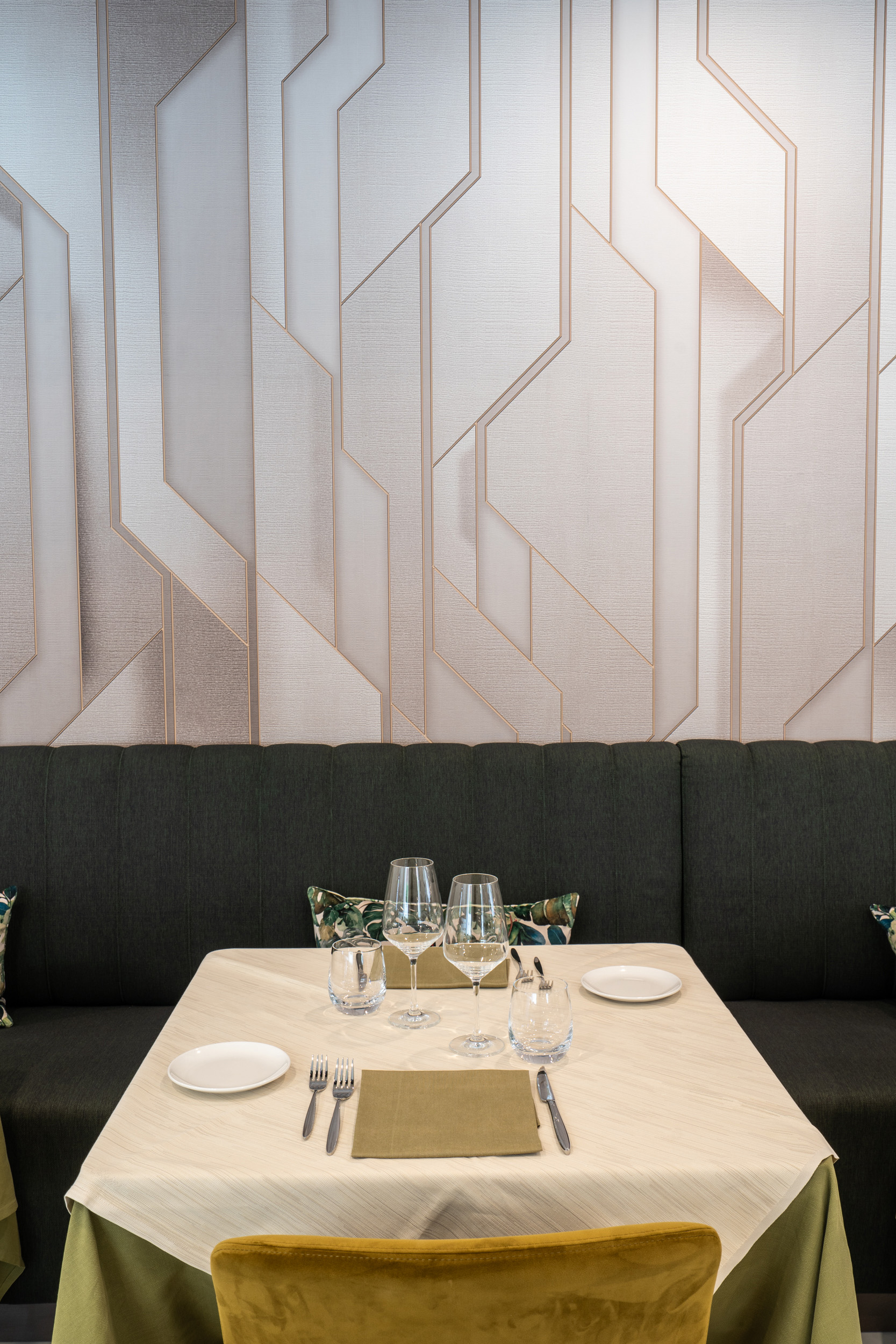 Modern restaurant table for two, geometric wall, green booth seating.
