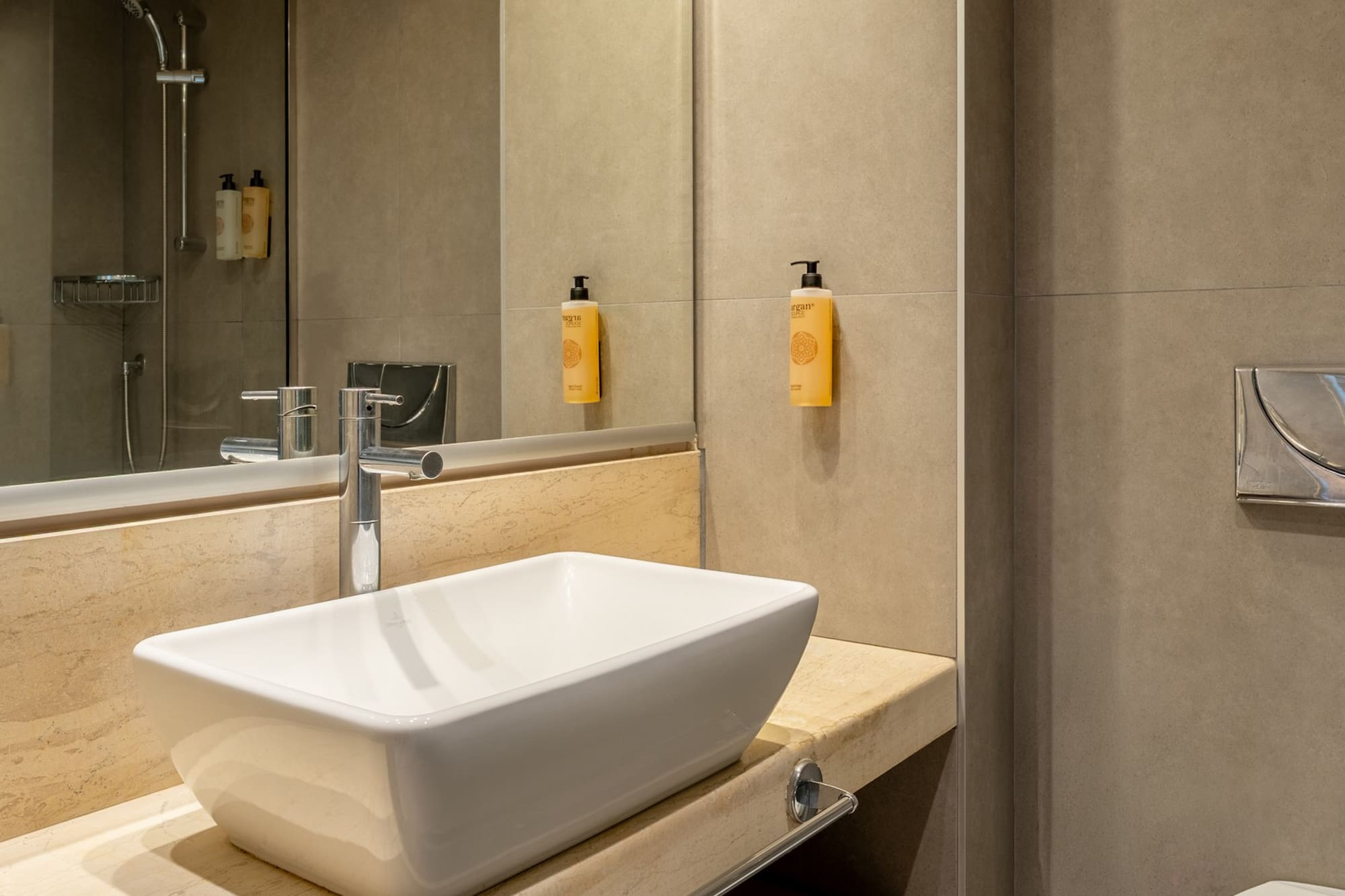 Modern bathroom with white vessel sink, marble vanity, shower, and toilet.