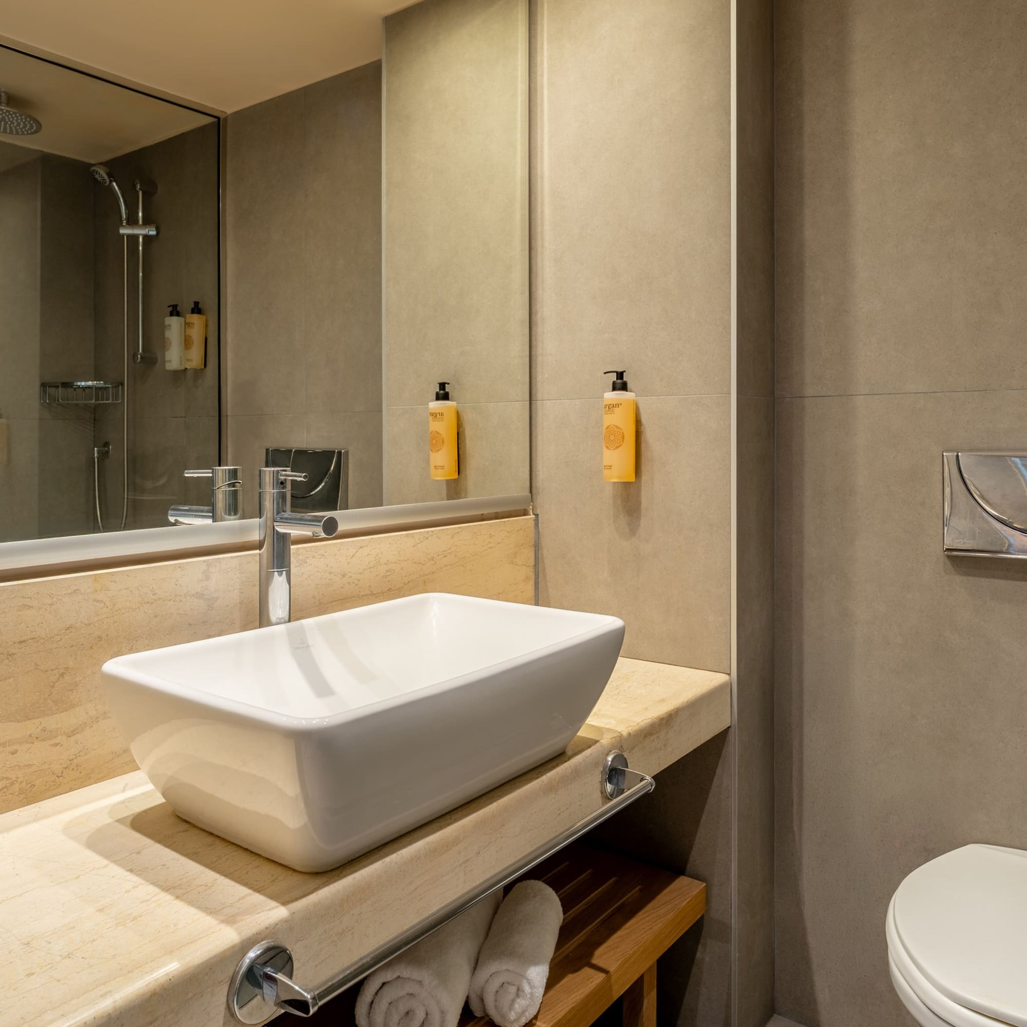 Modern bathroom with white vessel sink, marble vanity, shower, and toilet.