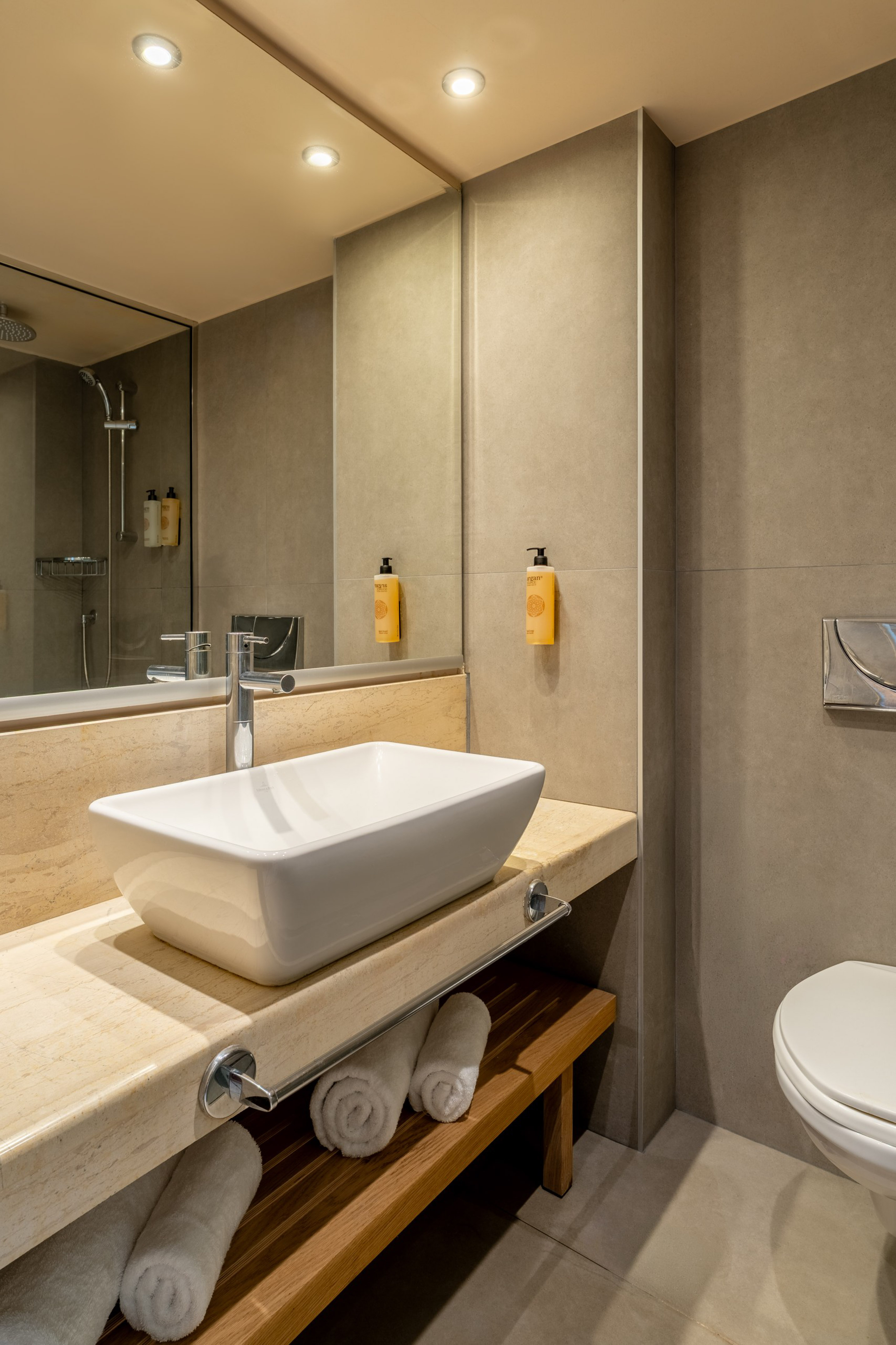 Modern bathroom with white vessel sink, marble vanity, shower, and toilet.