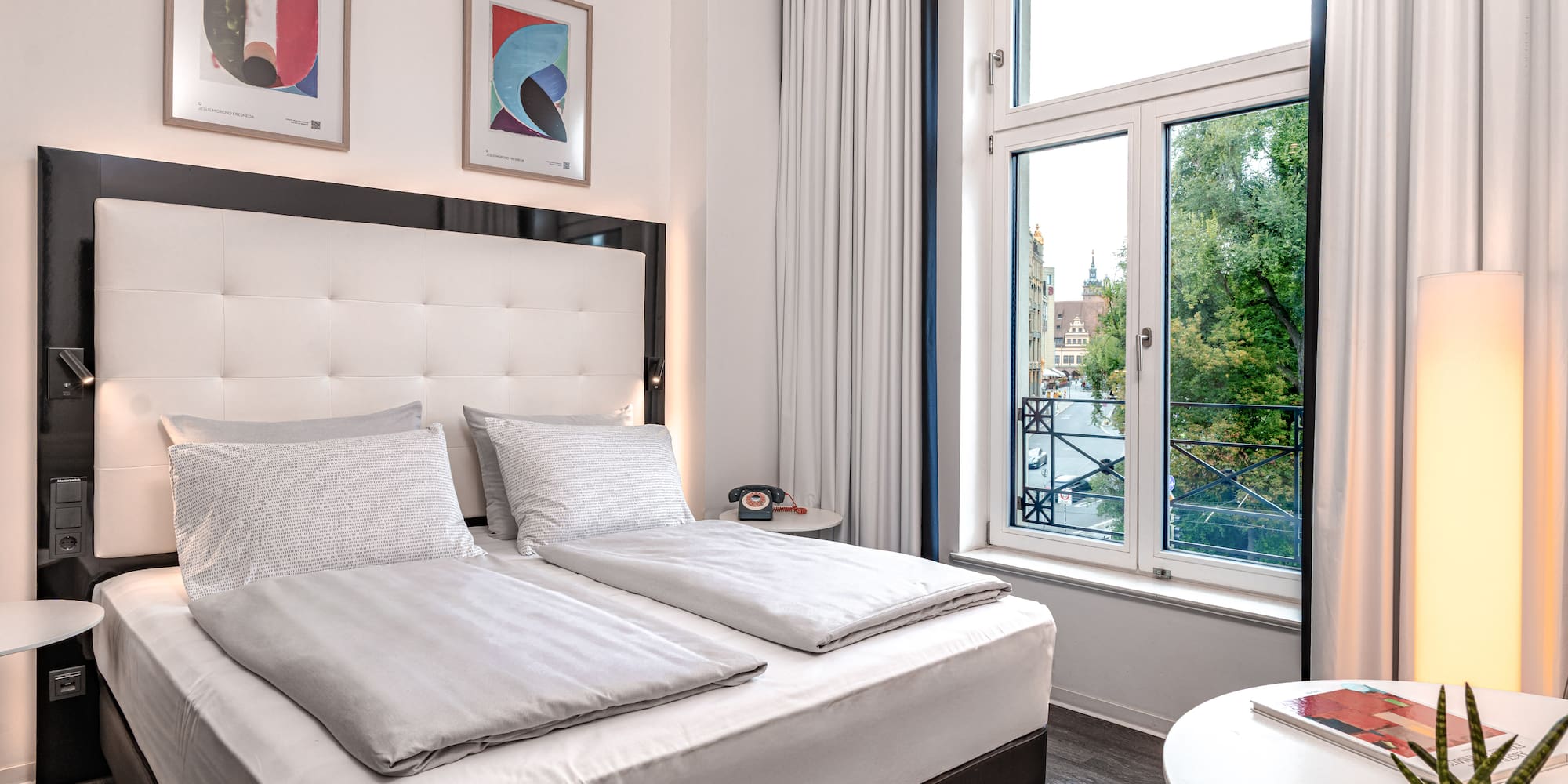 Stylish hotel room with large bed, modern decor, and city view from window.