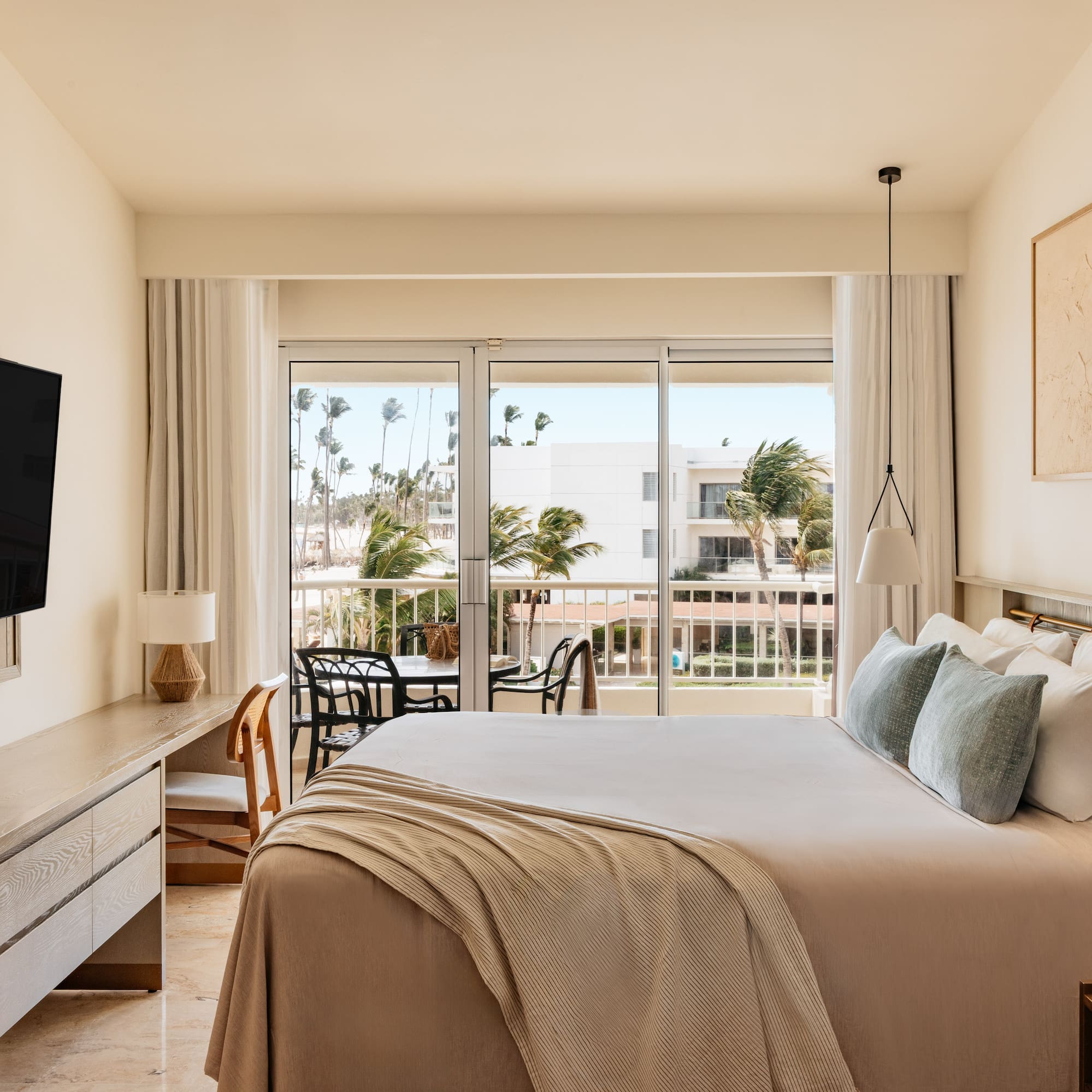 Contemporary hotel room with balcony, king bed, and tropical resort view.