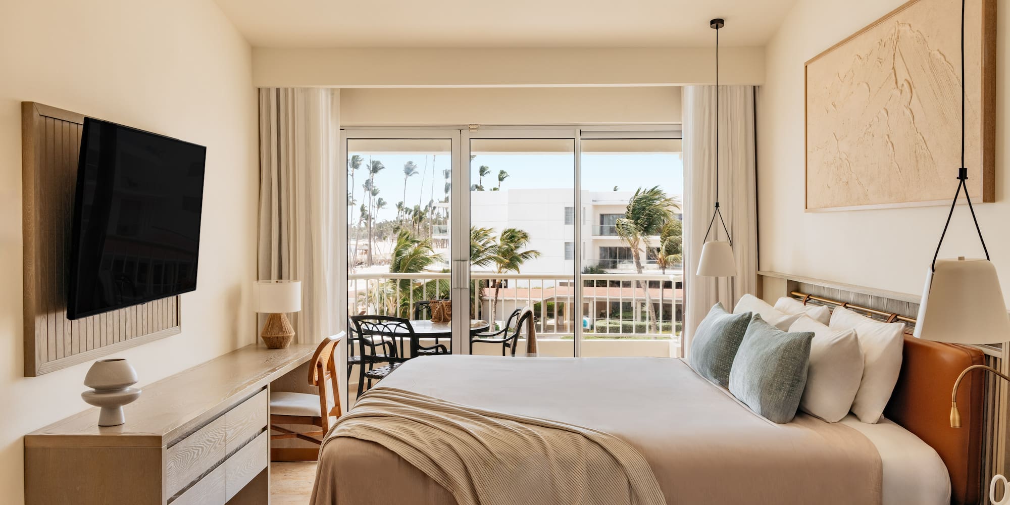 Contemporary hotel room with balcony, king bed, and tropical resort view.