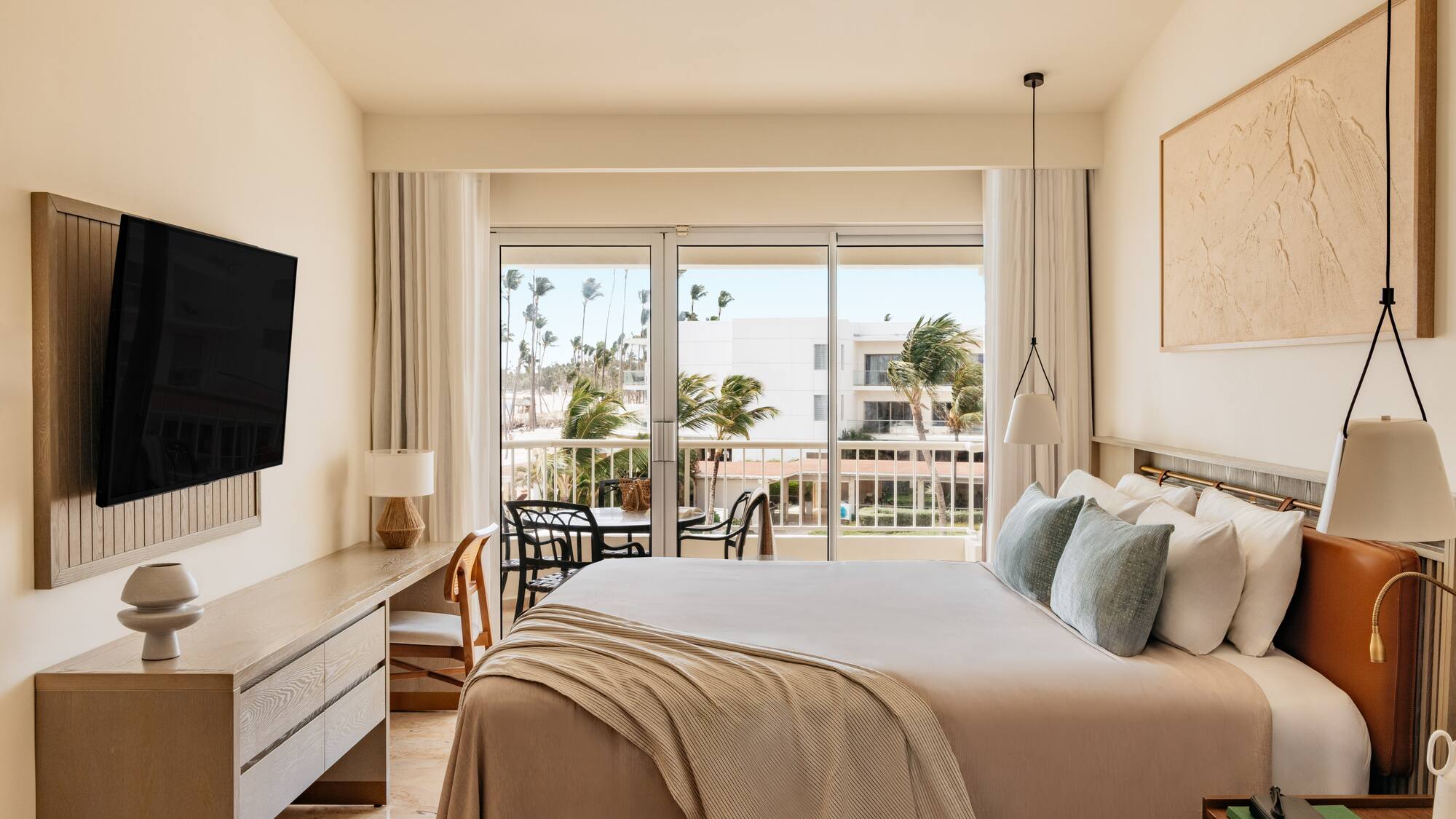 Contemporary hotel room with balcony, king bed, and tropical resort view.